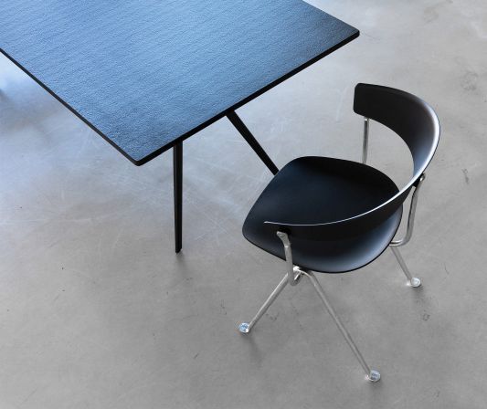 Schwarzer Officina Stuhl von Magis mit Stahlgestell neben einem schwarzen Tisch auf grauem Untergrund.