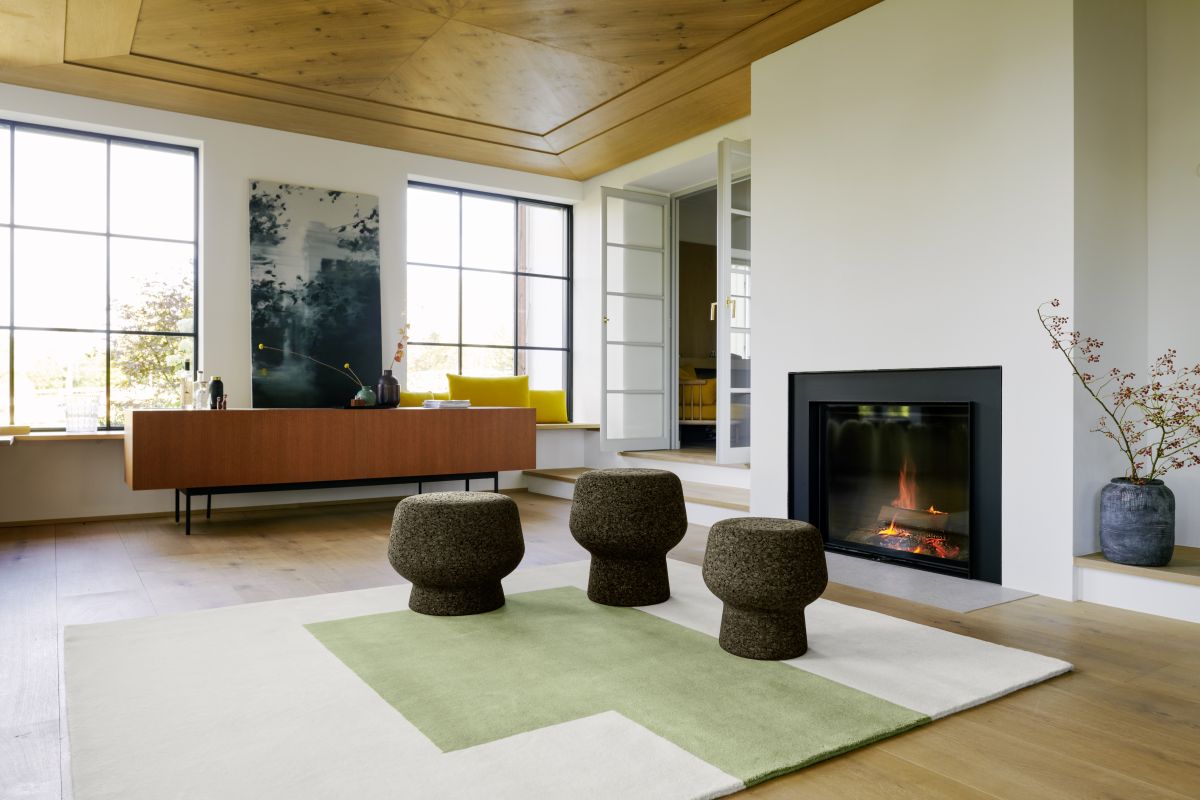Kilkenny Teppich 300x250cm von ClassiCon in modernem Wohnzimmer mit Kamin und Hockern.