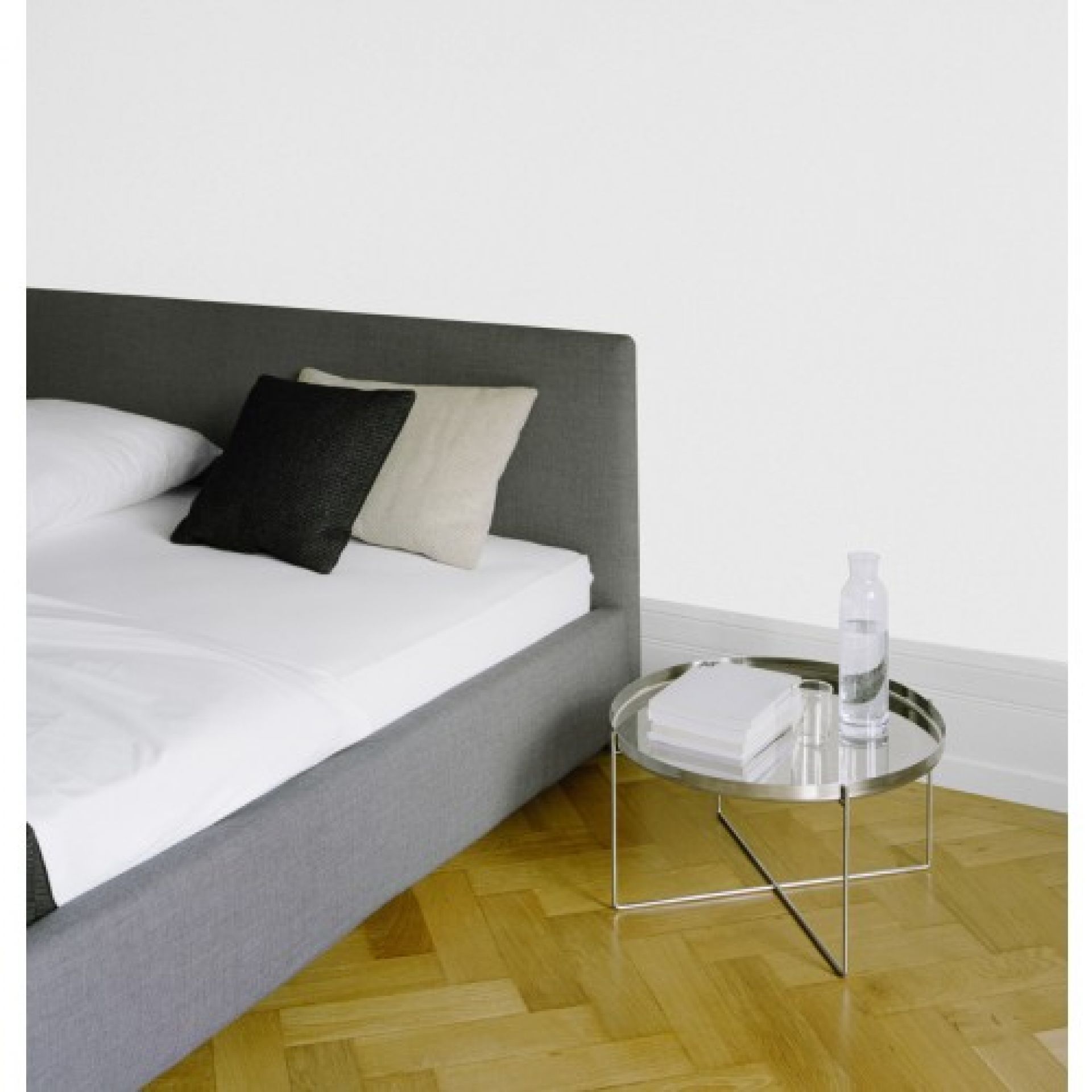 Habibi Beistelltisch von e15 im Schlafzimmer neben einem grauen Bett mit Kissen.