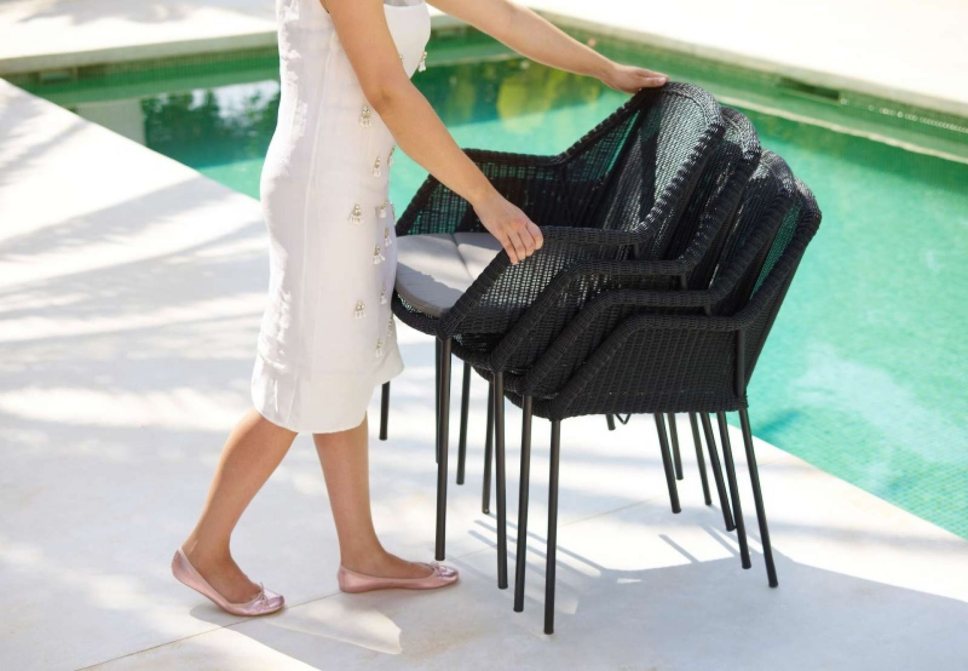 Stapel schwarzer Cane-Line Outdoor Stühle mit Breeze Kissen am Pool. Gartenmöbel.
