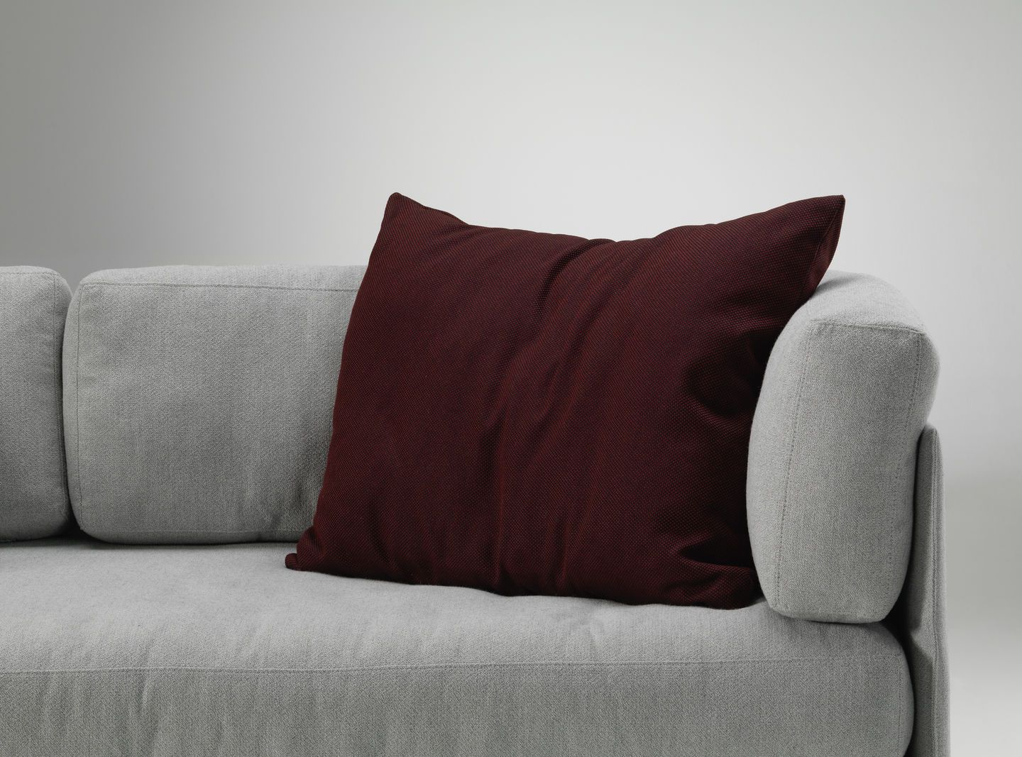 Vitra Kissen in Bordeauxrot auf einem grauen Sofa, modernes Wohnaccessoire für stilvolles Interieur.