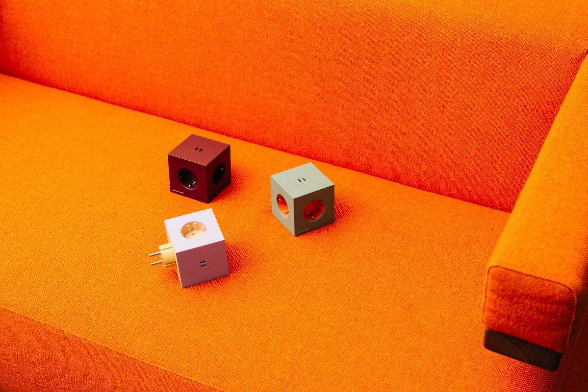 Drei Avolt Square 2 Steckdosenwürfel in Rot, Grün und Weiß auf einem orangefarbenen Sofa.