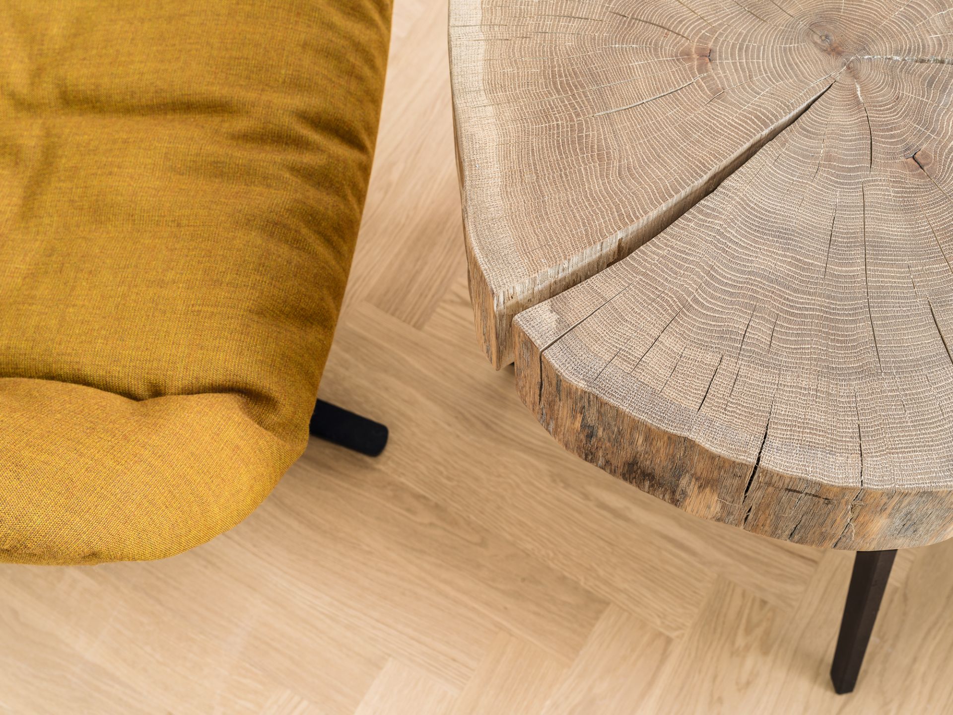 Detailaufnahme des Janua Stomp Beistelltisches H40 aus rohem Holz mit Baumscheiben-Tischplatte neben einem gelben Sessel.