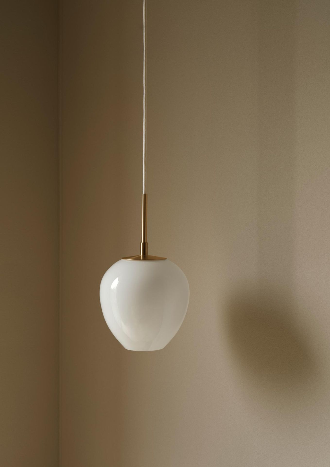 Weiße Tulip Pendelleuchte von Carl Hansen & Søn mit Messingdetails vor beiger Wand.