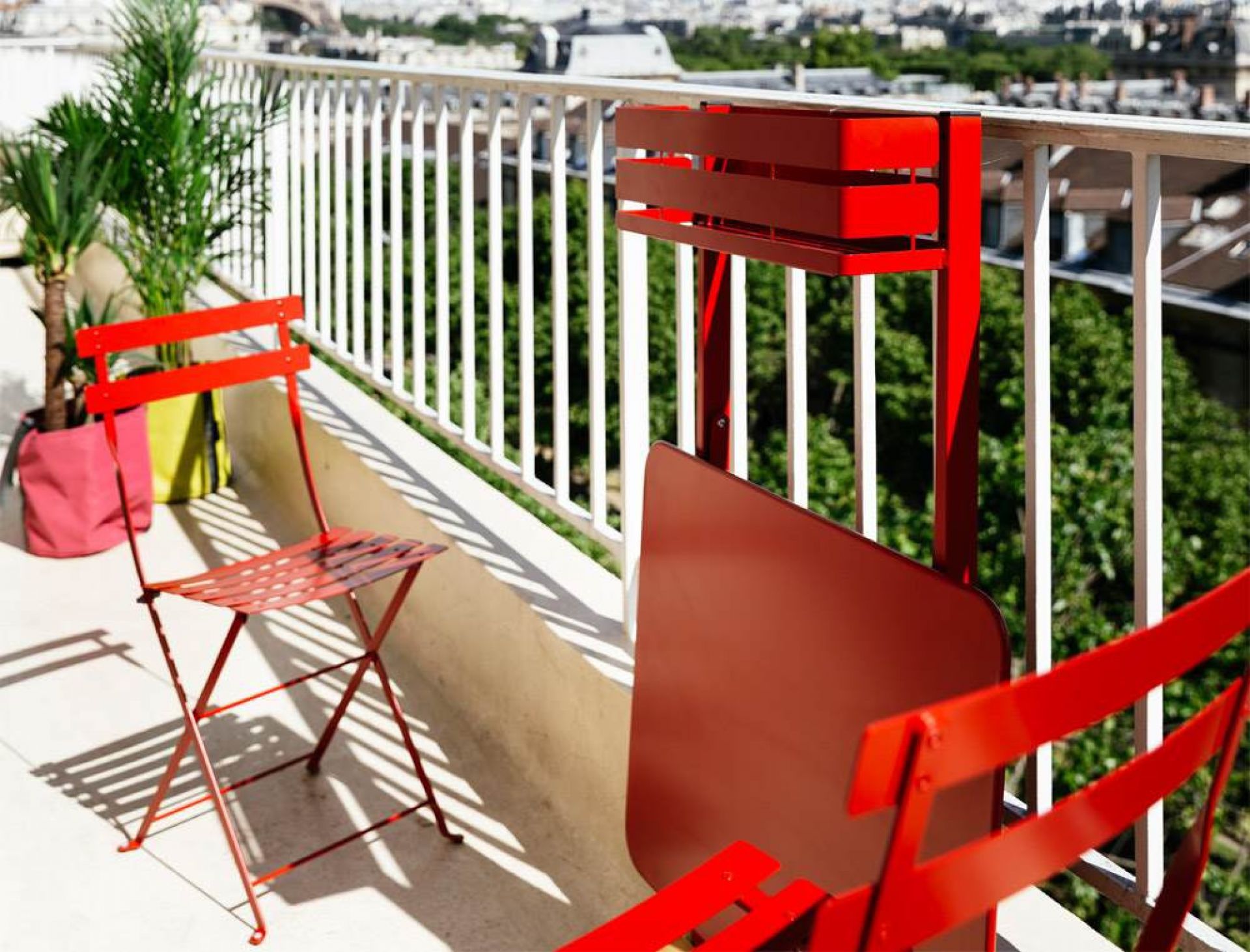 Roter Bistro Balkontisch und Stühle von Fermob auf einem sonnigen Balkon mit Ausblick.