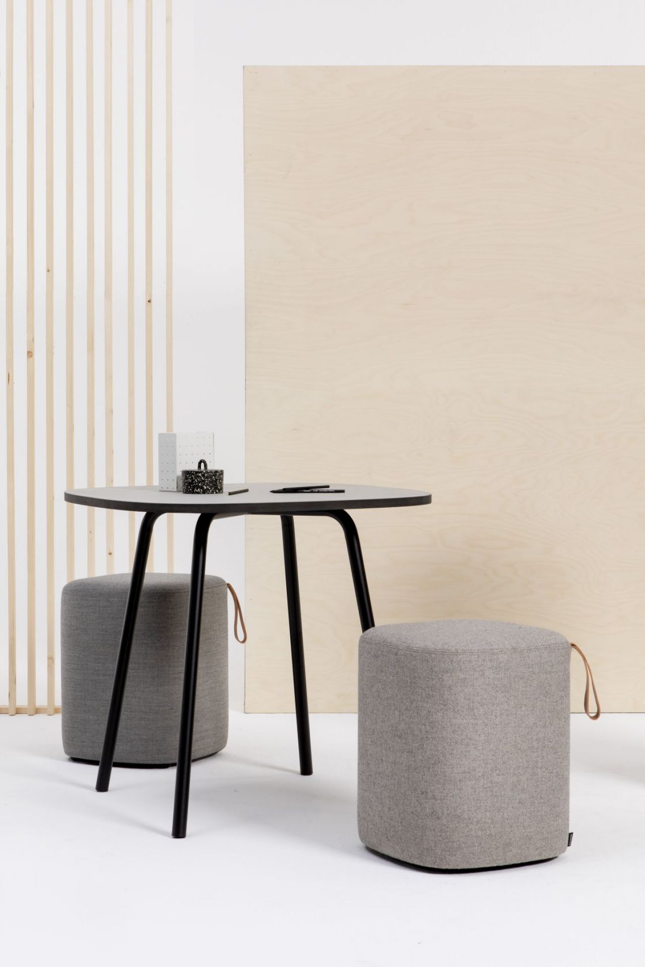 Grauer Pully Hocker von Cascando neben einem Tisch, ideal als Sitzgelegenheit für Büro und Wartebereich.