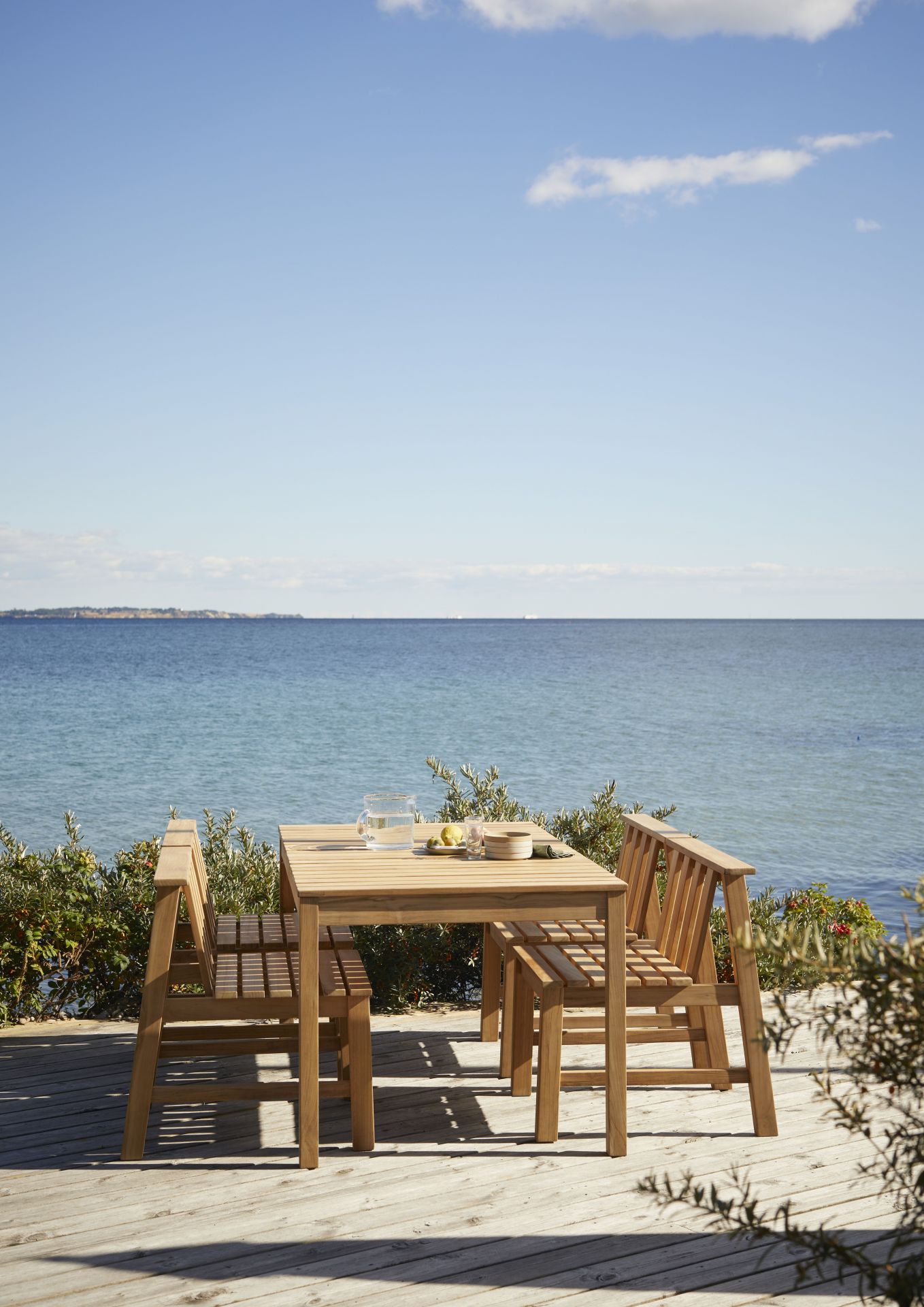 Cadence Teak Stühle und Tisch von Skagerak by Fritz Hansen auf Holzterrasse mit Meerblick.