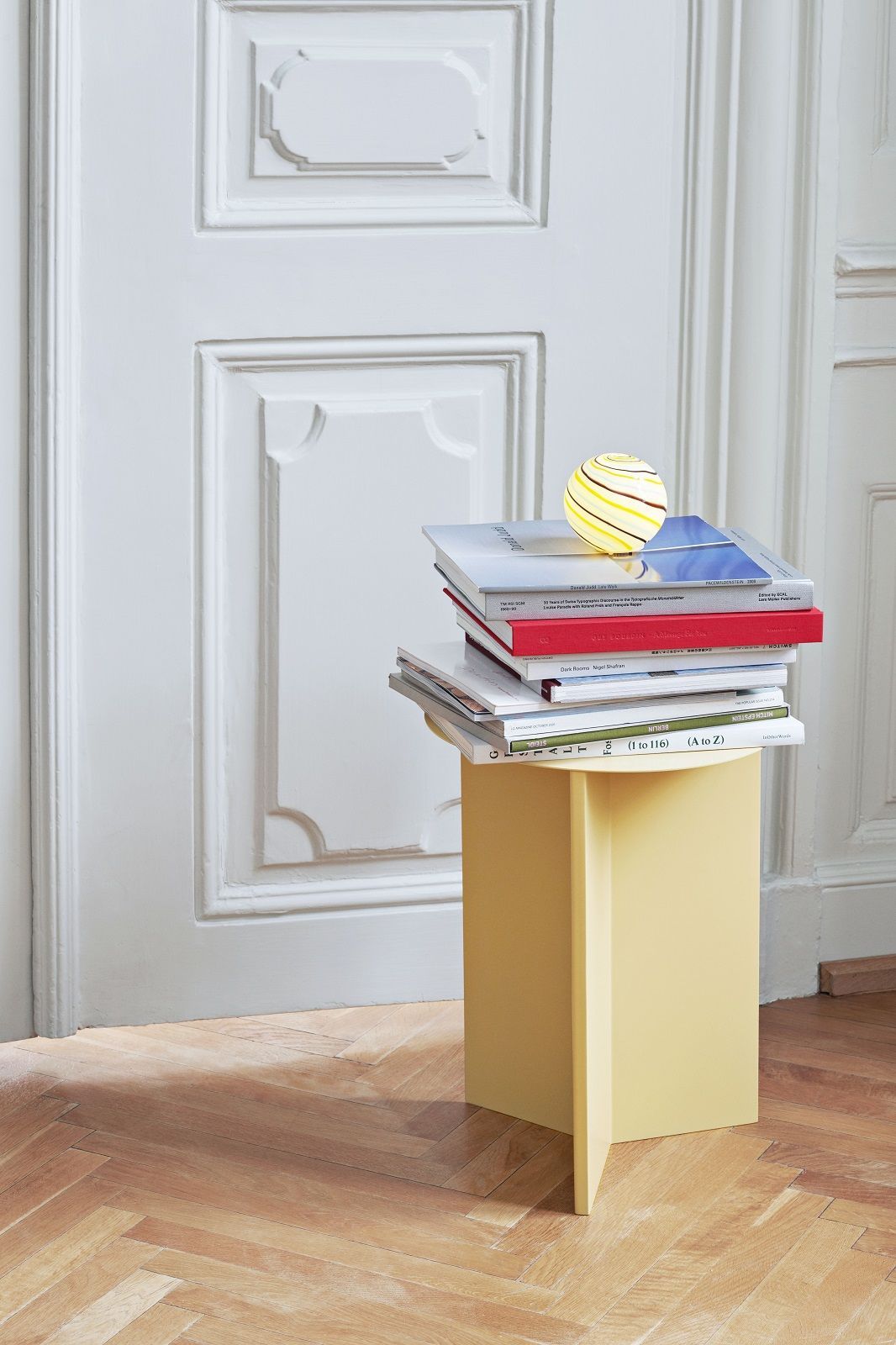 Gelber Hay Slit Table Beistelltisch mit Büchern und einer Lampe vor einer weißen Tür.