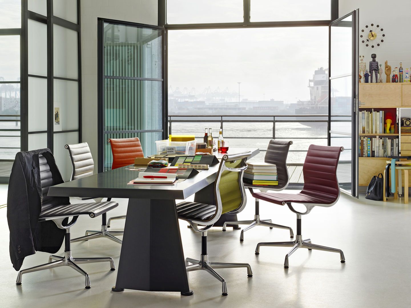 Konferenzraum mit schwarzem Tisch und mehreren Vitra EA 104 Aluminium Stühlen in verschiedenen Farben.