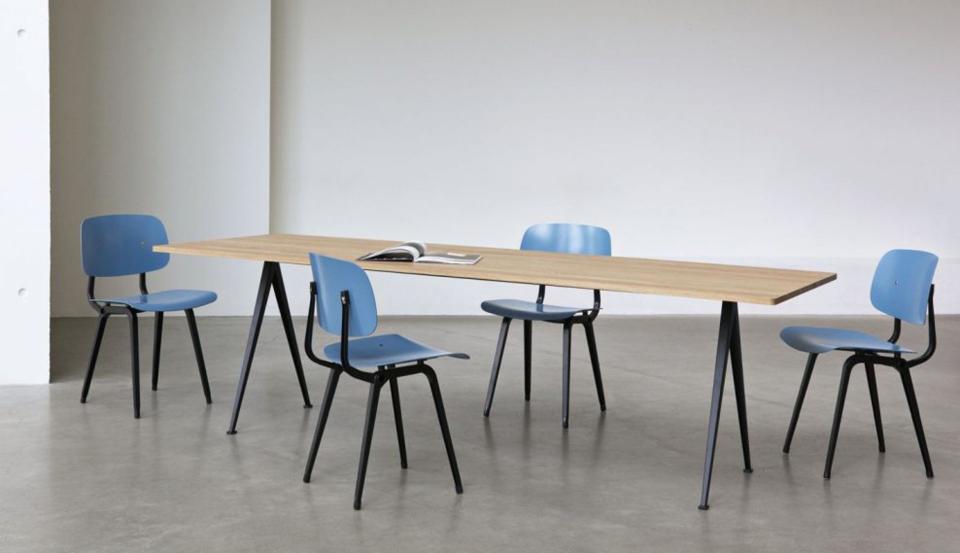 Vier blaue Hay Revolt Chair Stühle um einen Holztisch mit schwarzen Beinen, minimalistisches Design.
