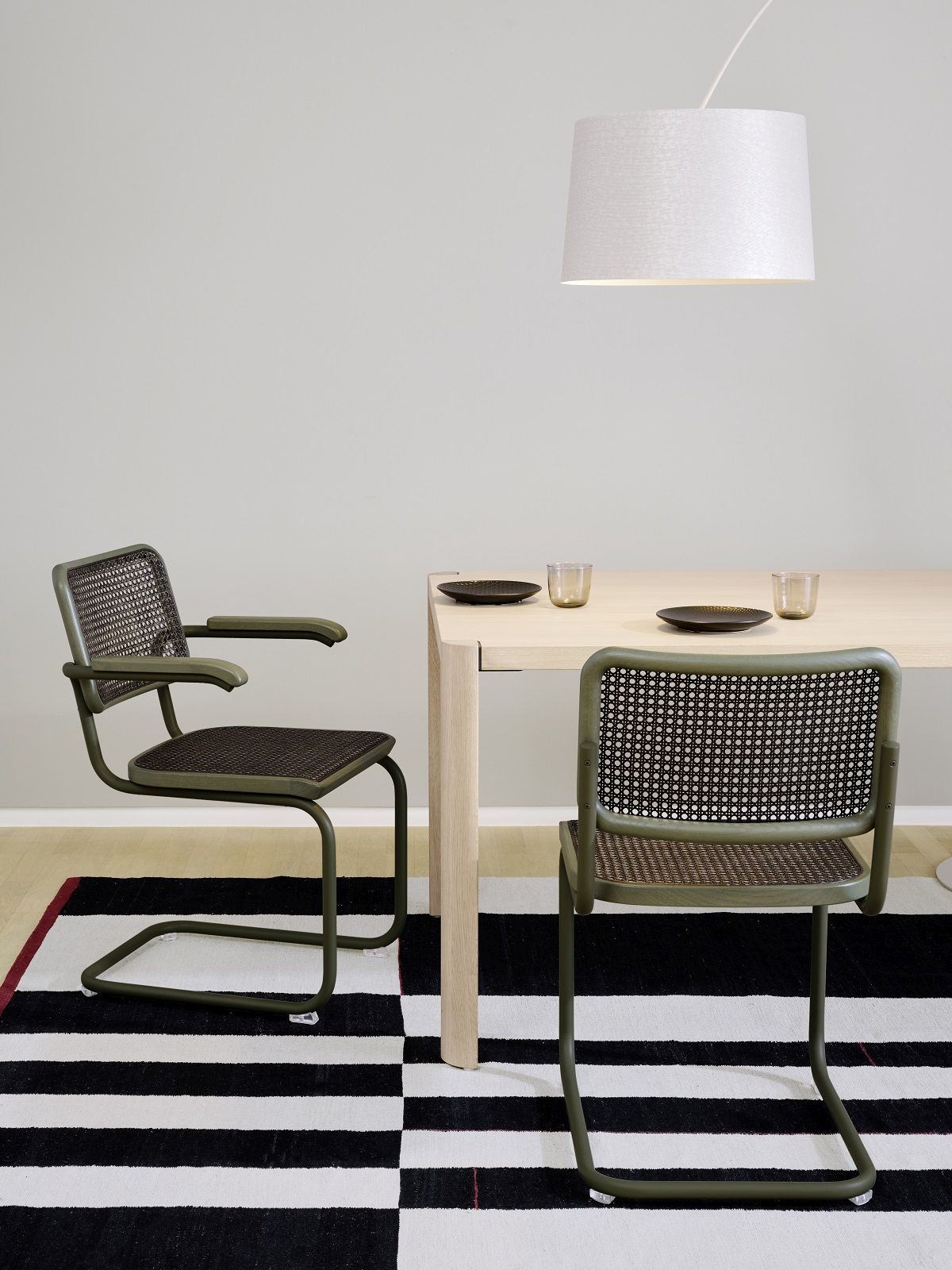 Zwei grüne S 32 Freischwinger Stühle von Thonet mit Rohrgeflecht an einem Esstisch.
