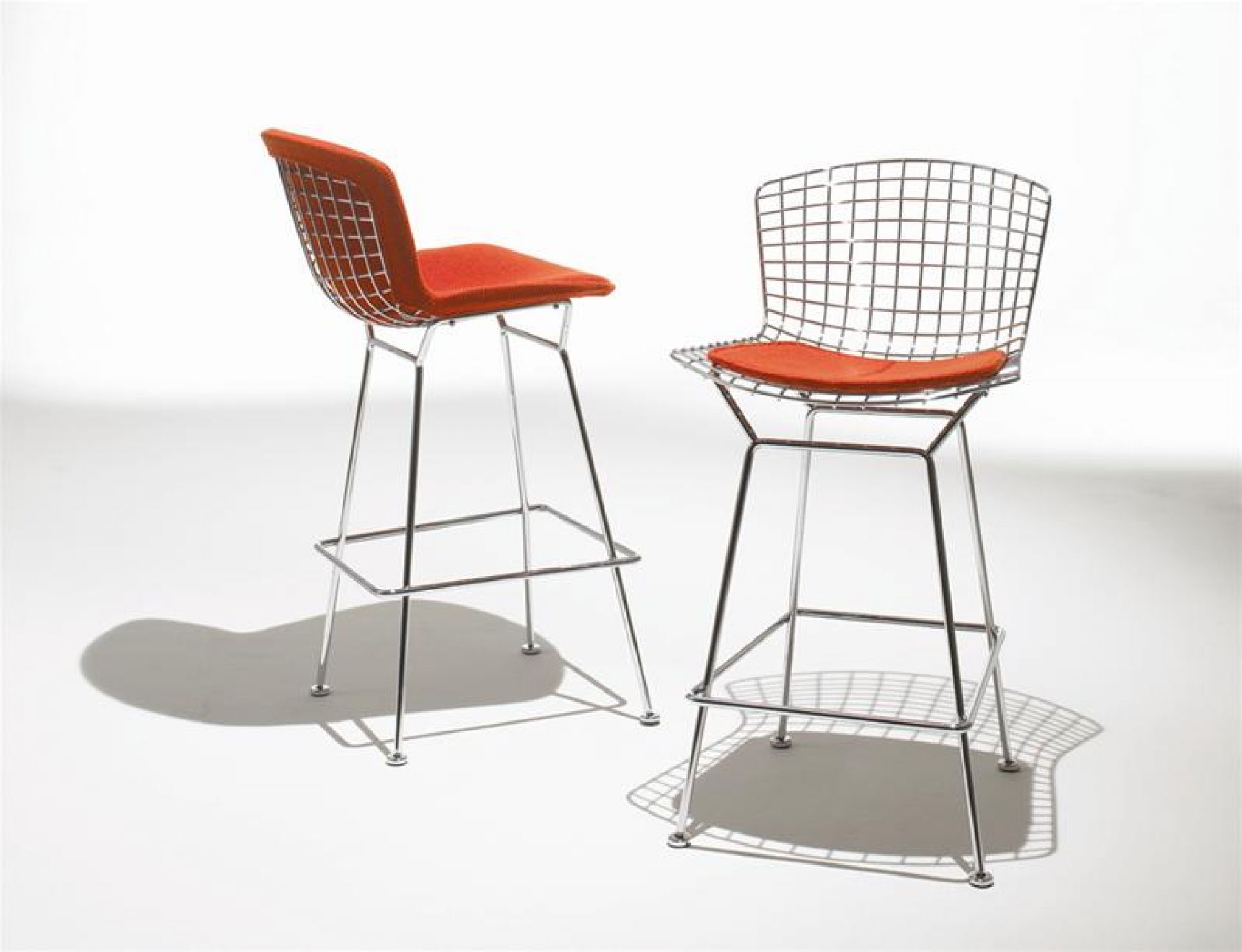 Zwei Bertoia Barhocker von Knoll International mit orangefarbenen Sitzkissen und verchromtem Drahtgestell.