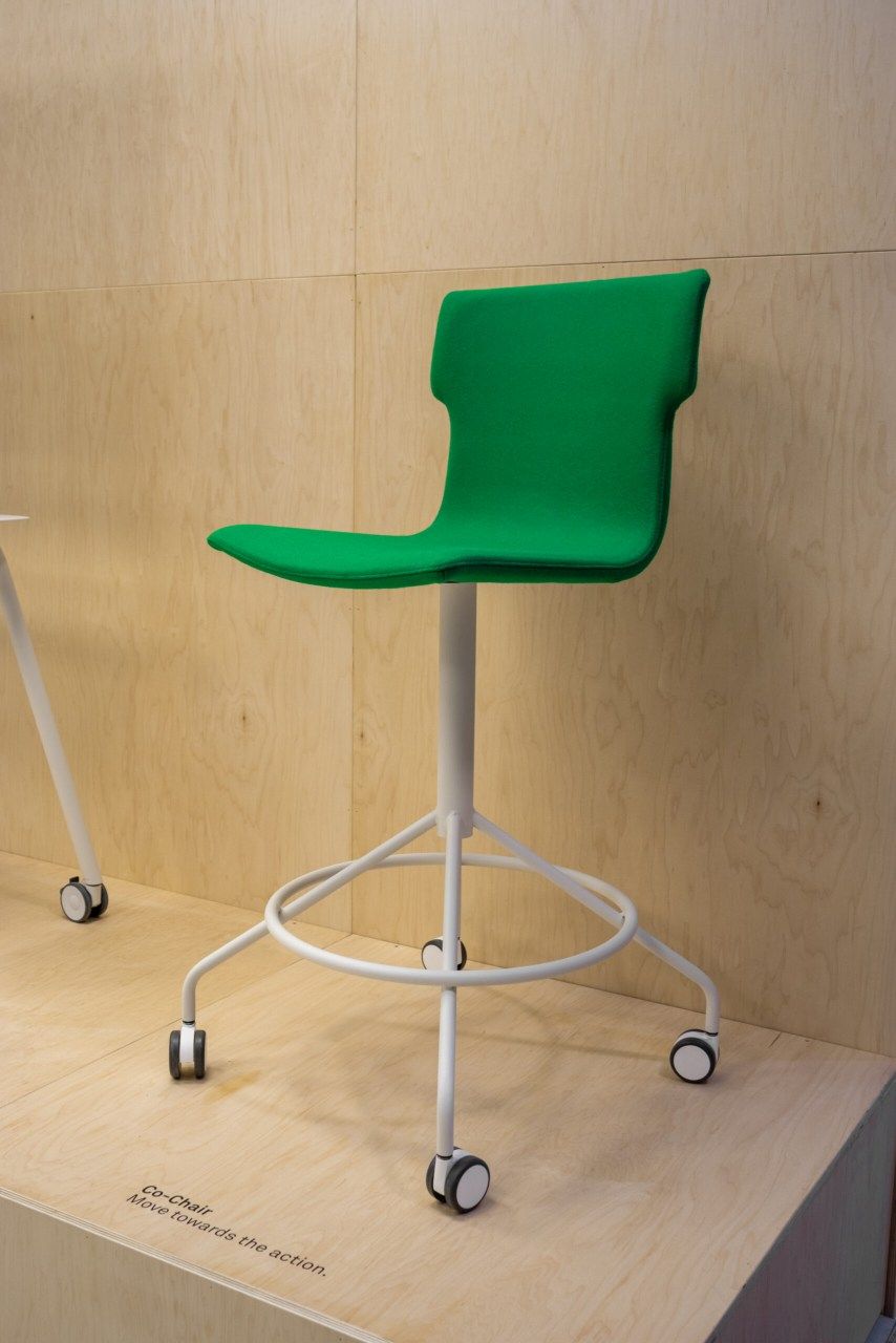 Co-Chair Bürodrehstuhl Cascando, grüner ergonomischer Hocker mit Rollen und weißem Gestell vor Holzwand.