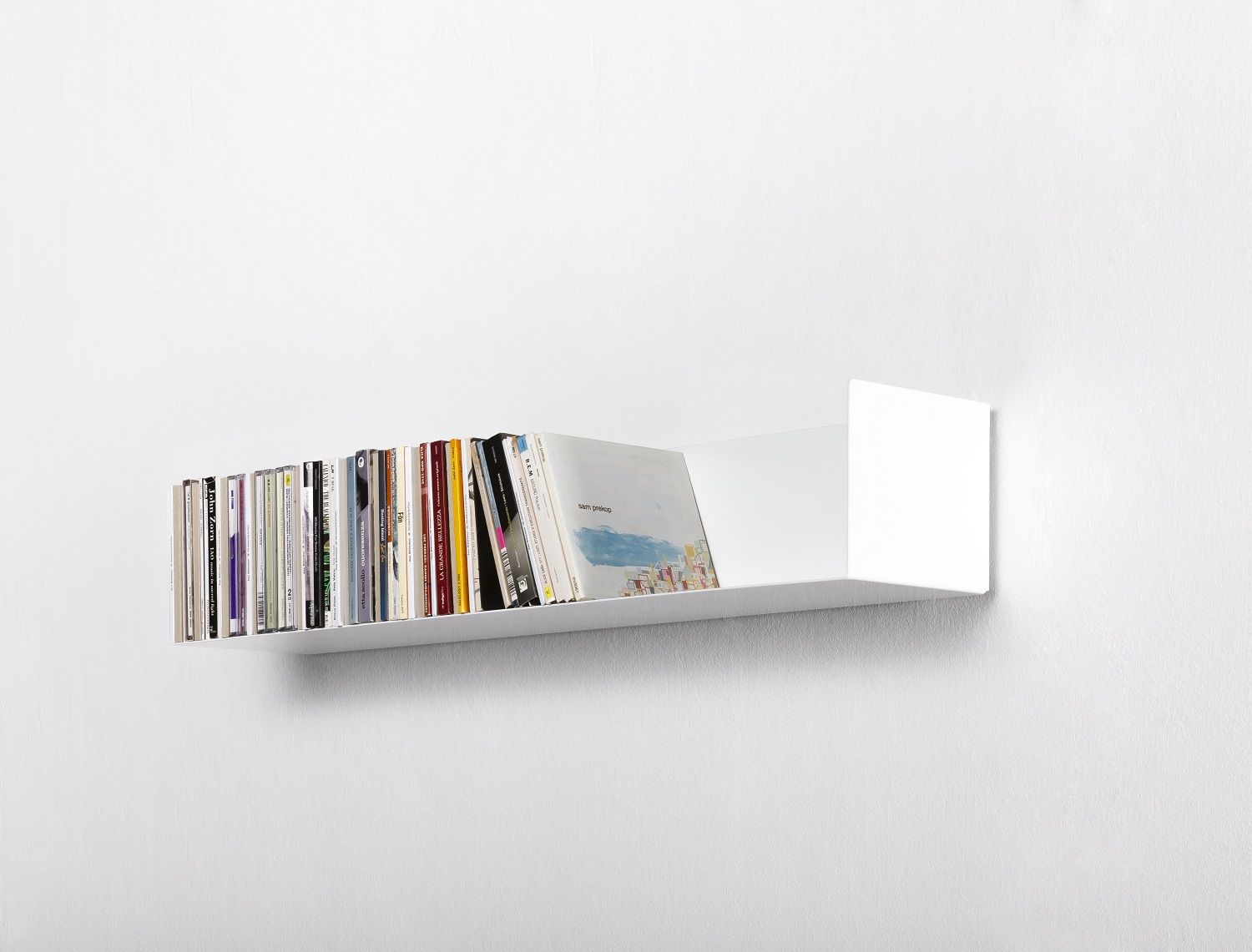 Weißes CD-Regal Linea1 von Müller Möbelwerkstätten an einer weißen Wand, gefüllt mit CDs.