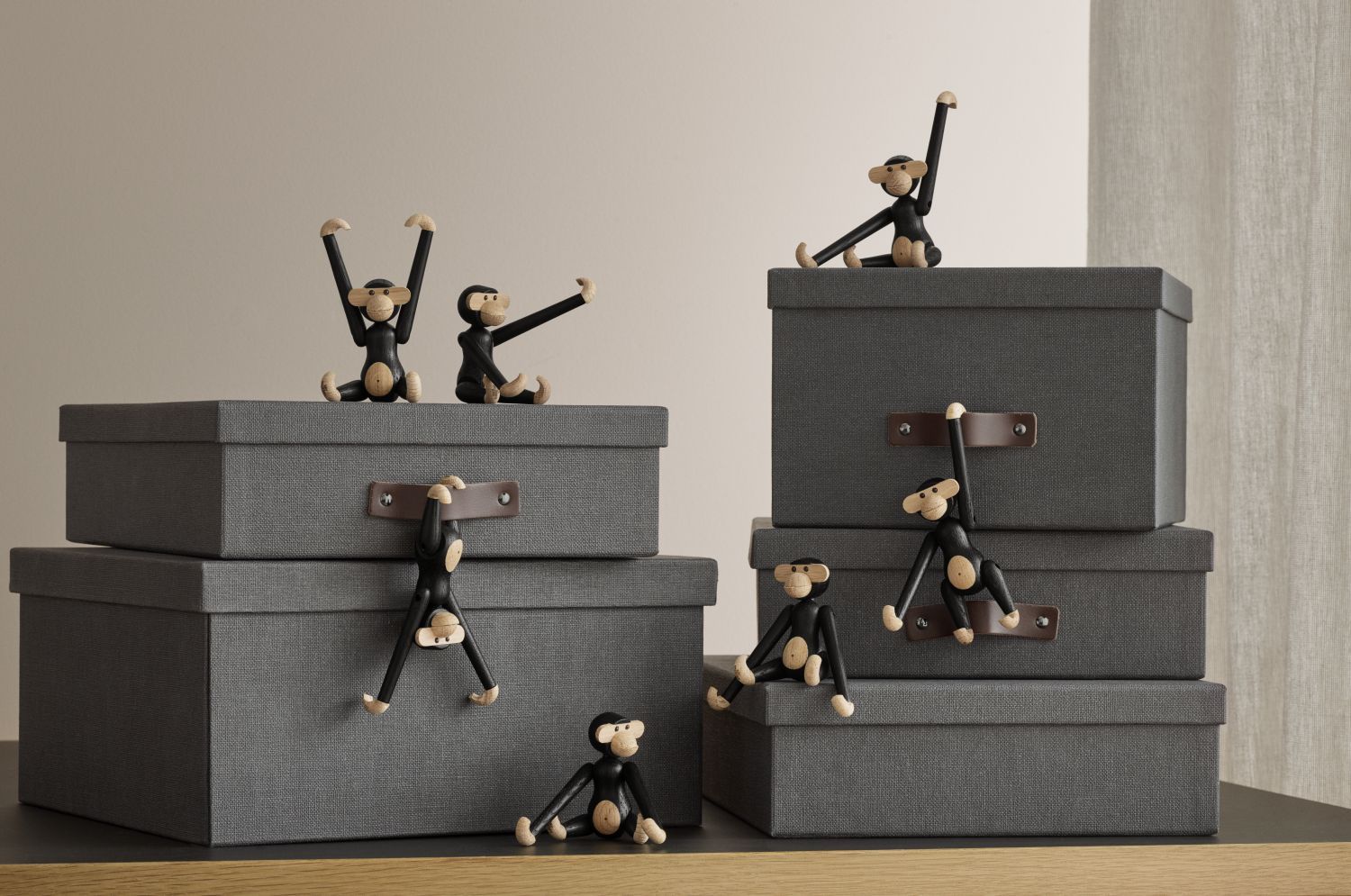 Mehrere Kay Bojesen Holzfiguren, Affen Minis, sitzen und hängen an grauen Stoffboxen.