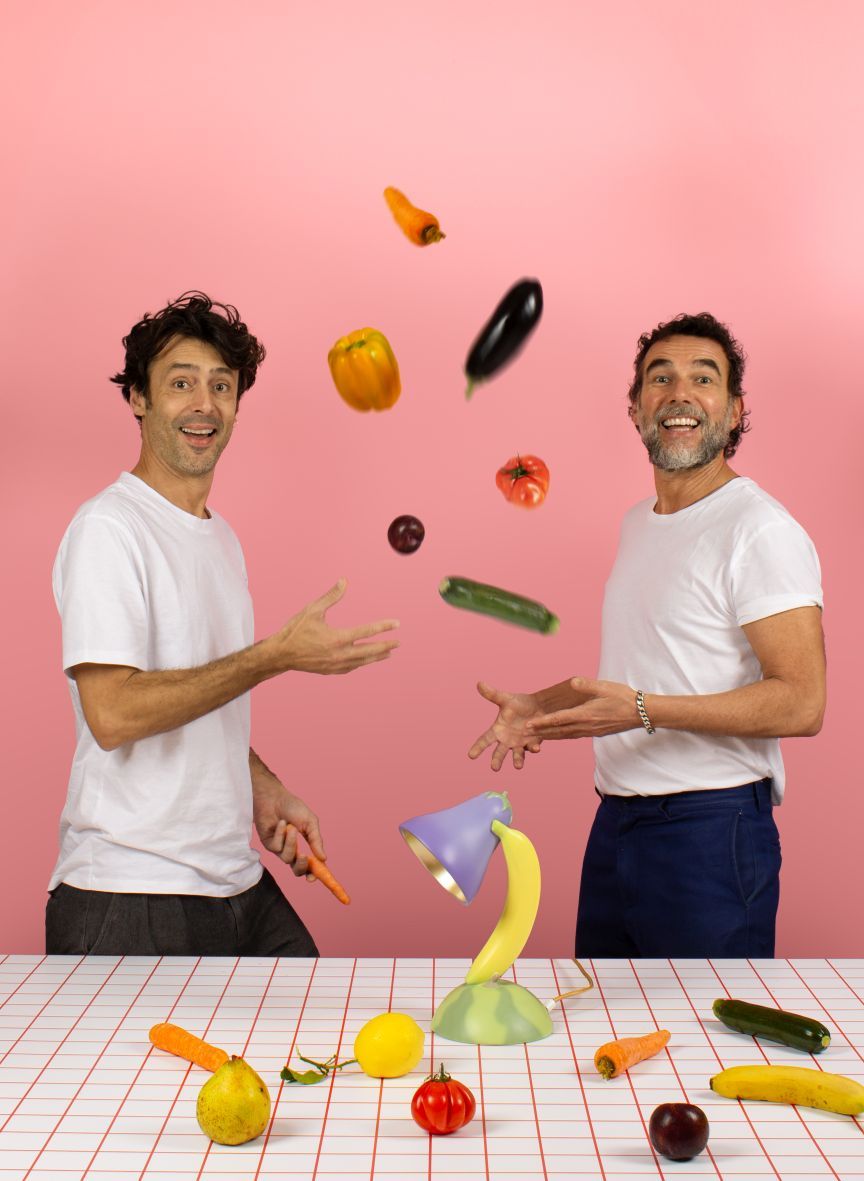 Vitamin Table Lamp Aubergine von Seletti mit jonglierenden Männern und Gemüse vor rosa Hintergrund.