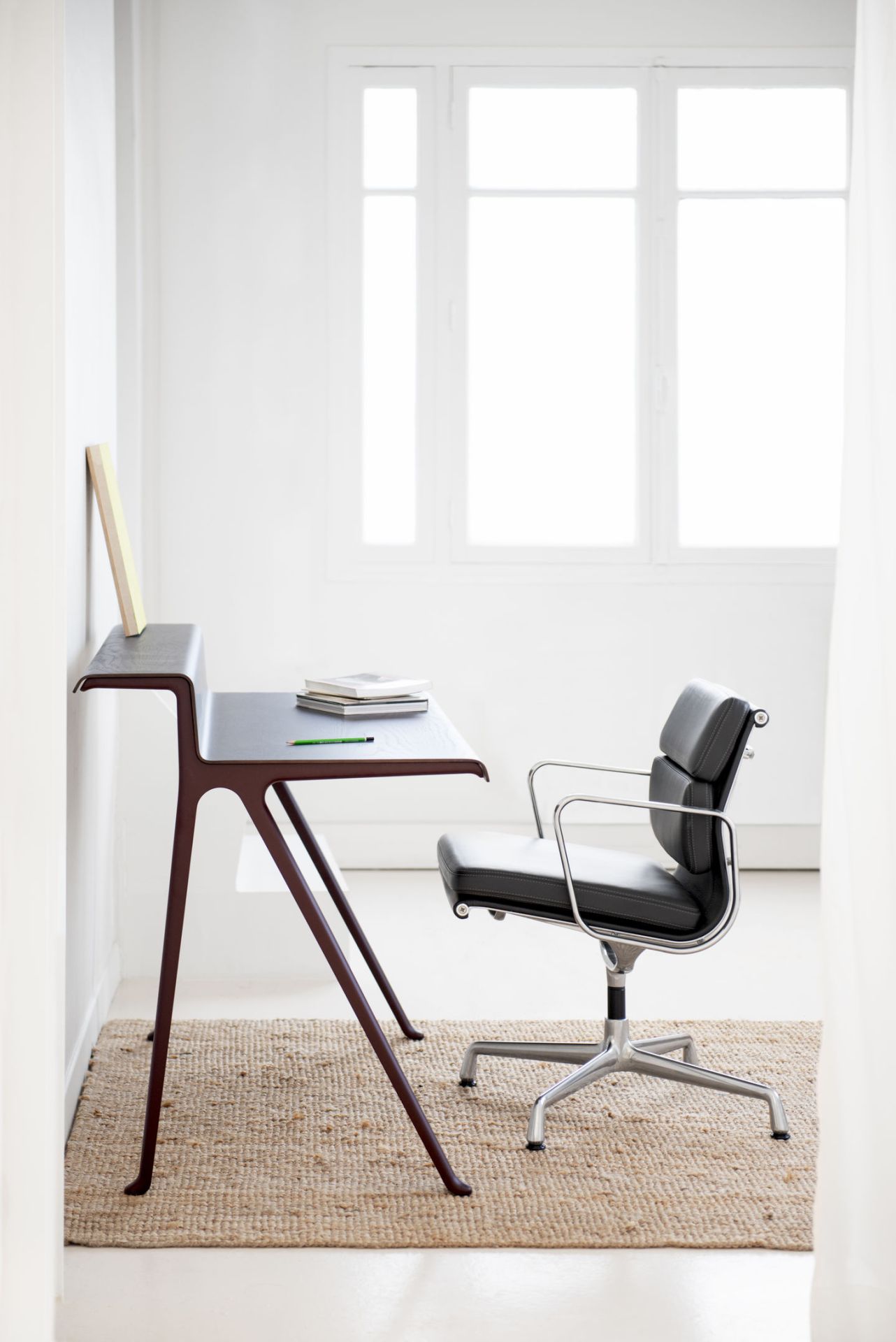 Vitra Courier Schreibtisch mit schwarzer Bürostuhl auf einem Teppich in einem hellen Raum.