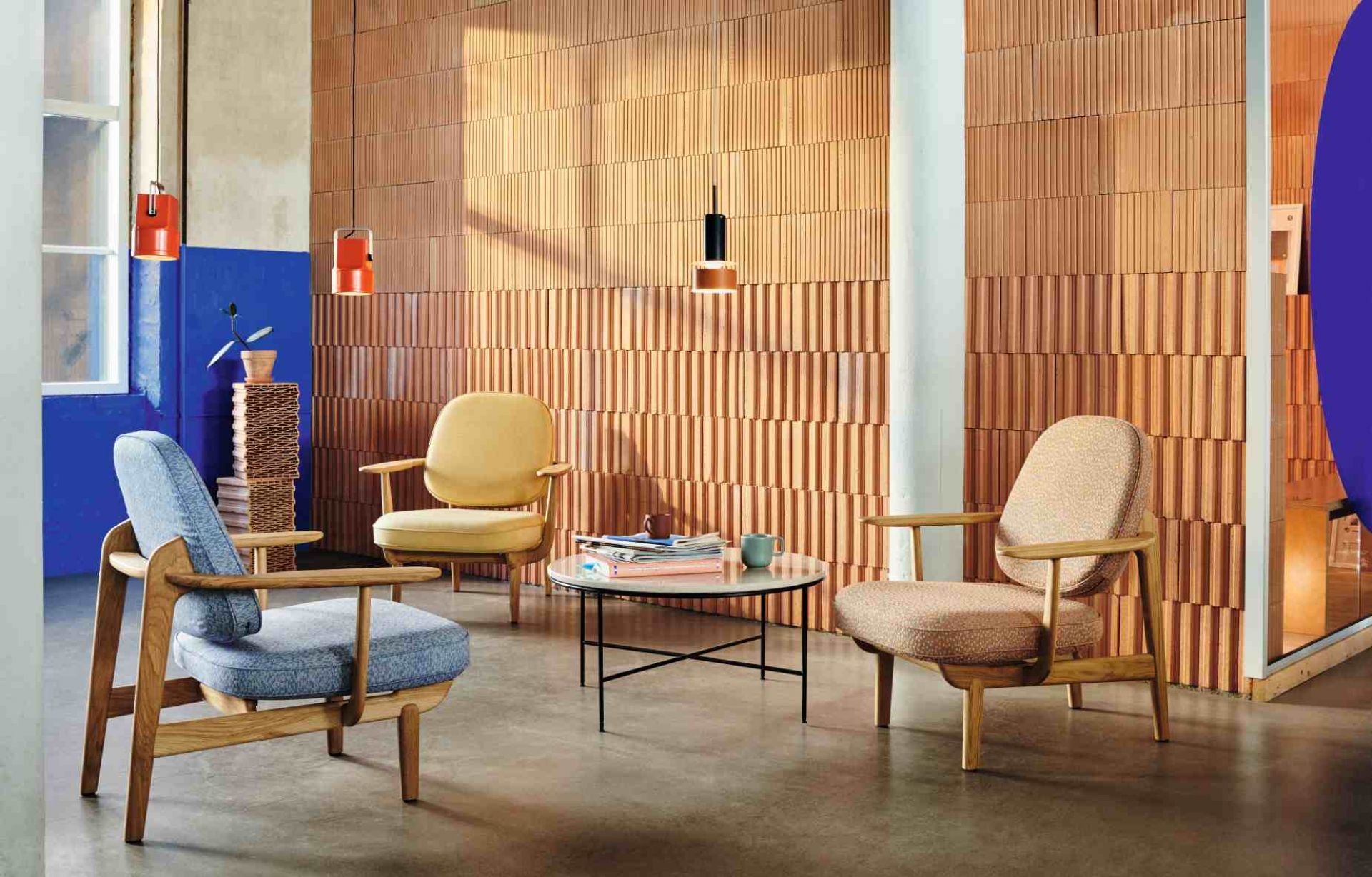 Interieur mit drei Fritz Hansen Fred Loungesesseln in Gelb, Blau und Beige um einen Tisch.