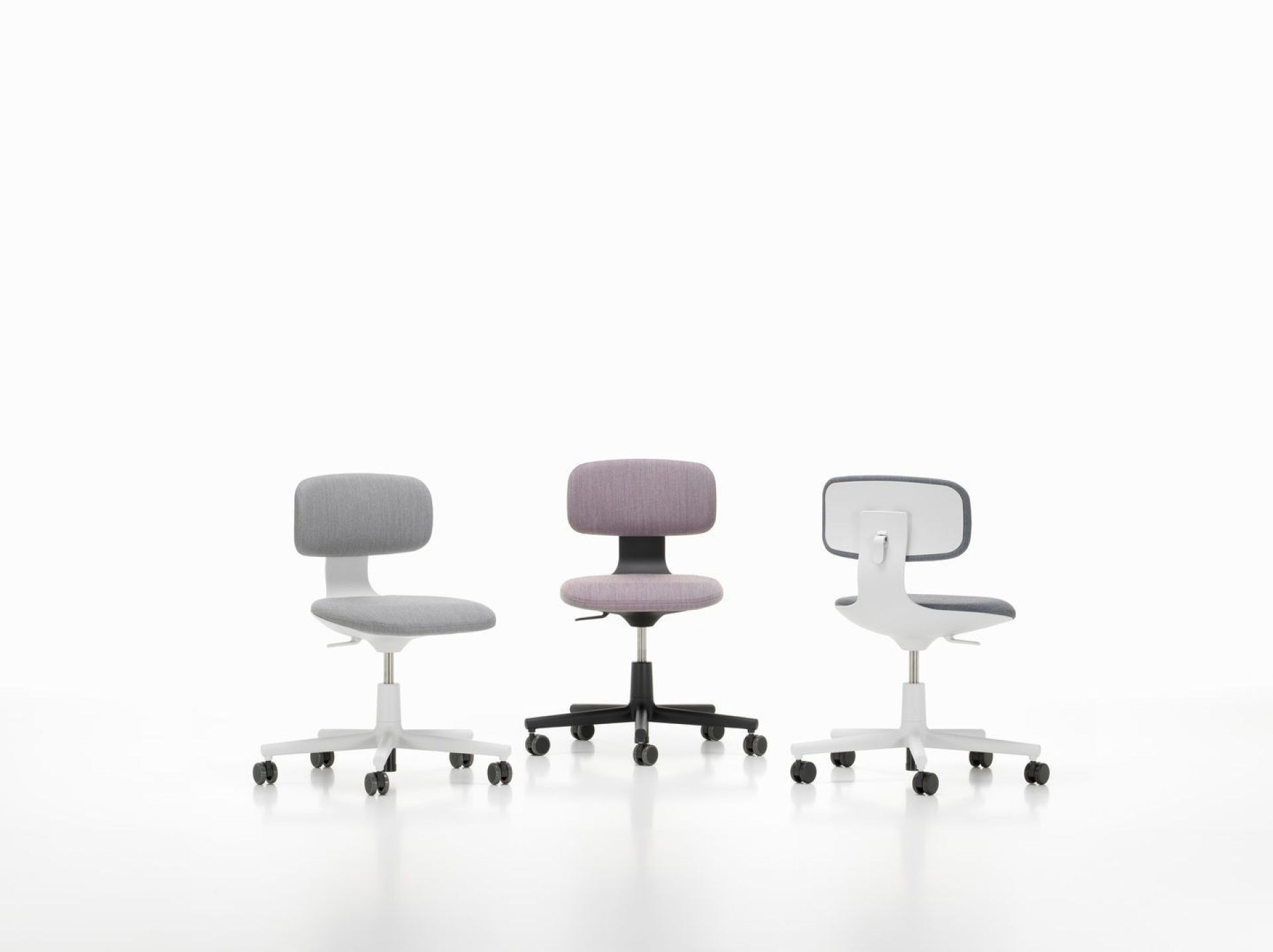 Drei Vitra Rookie Bürodrehstühle in Grau, Lila und Weiß mit Rollen vor einem weißen Hintergrund.