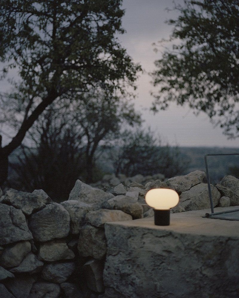 Karl-Johan Akkuleuchte von New Works, portable Tischlampe im Außenbereich auf Steinmauer.
