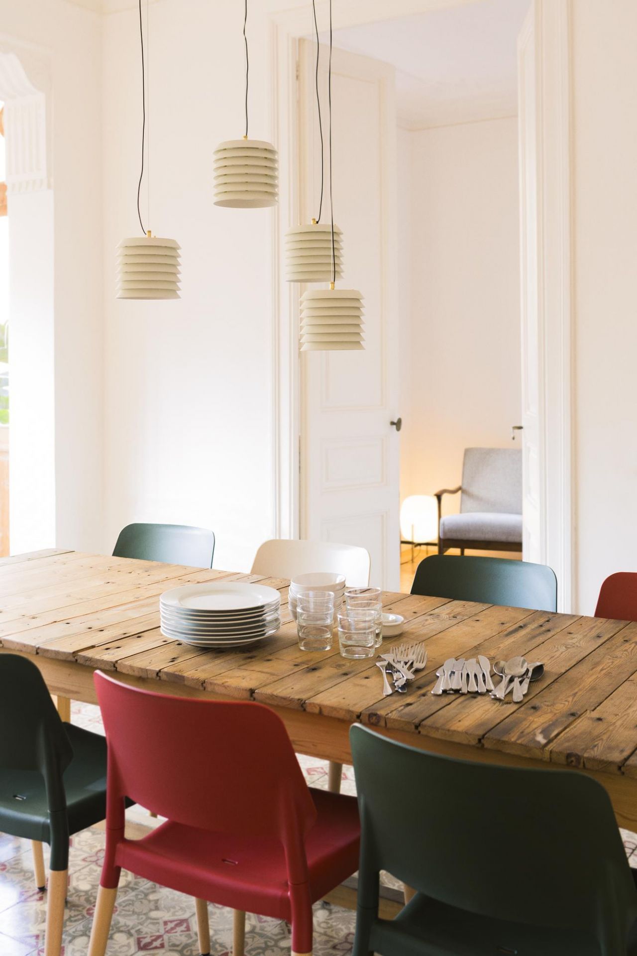 Esstisch aus Holz mit Tellern, Gläsern, Besteck und bunten Stühlen unter modernen Hängelampen im Esszimmer.