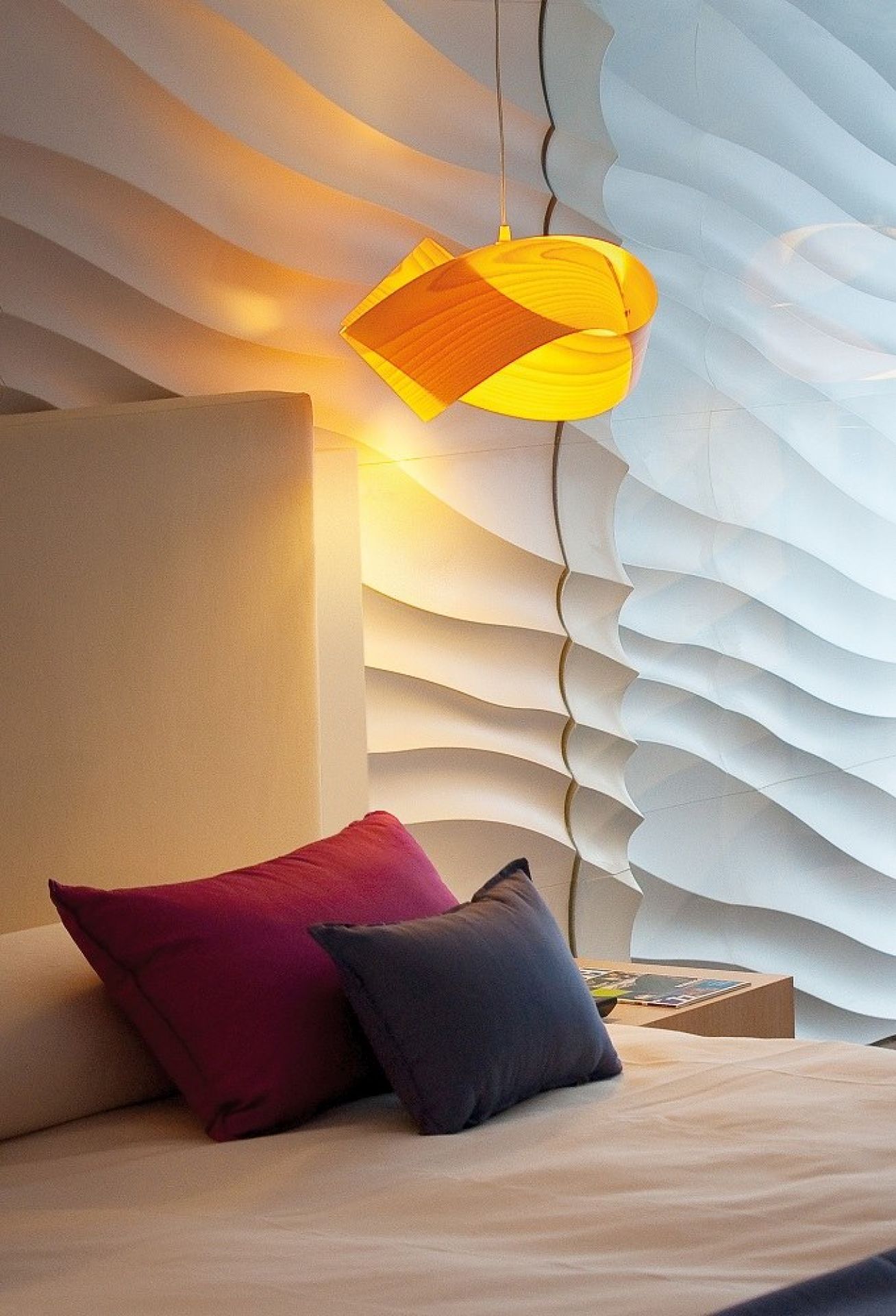 Orangefarbene Nut Pendelleuchte von LZF Lamps über einem Bett mit Kissen. Designlampe.