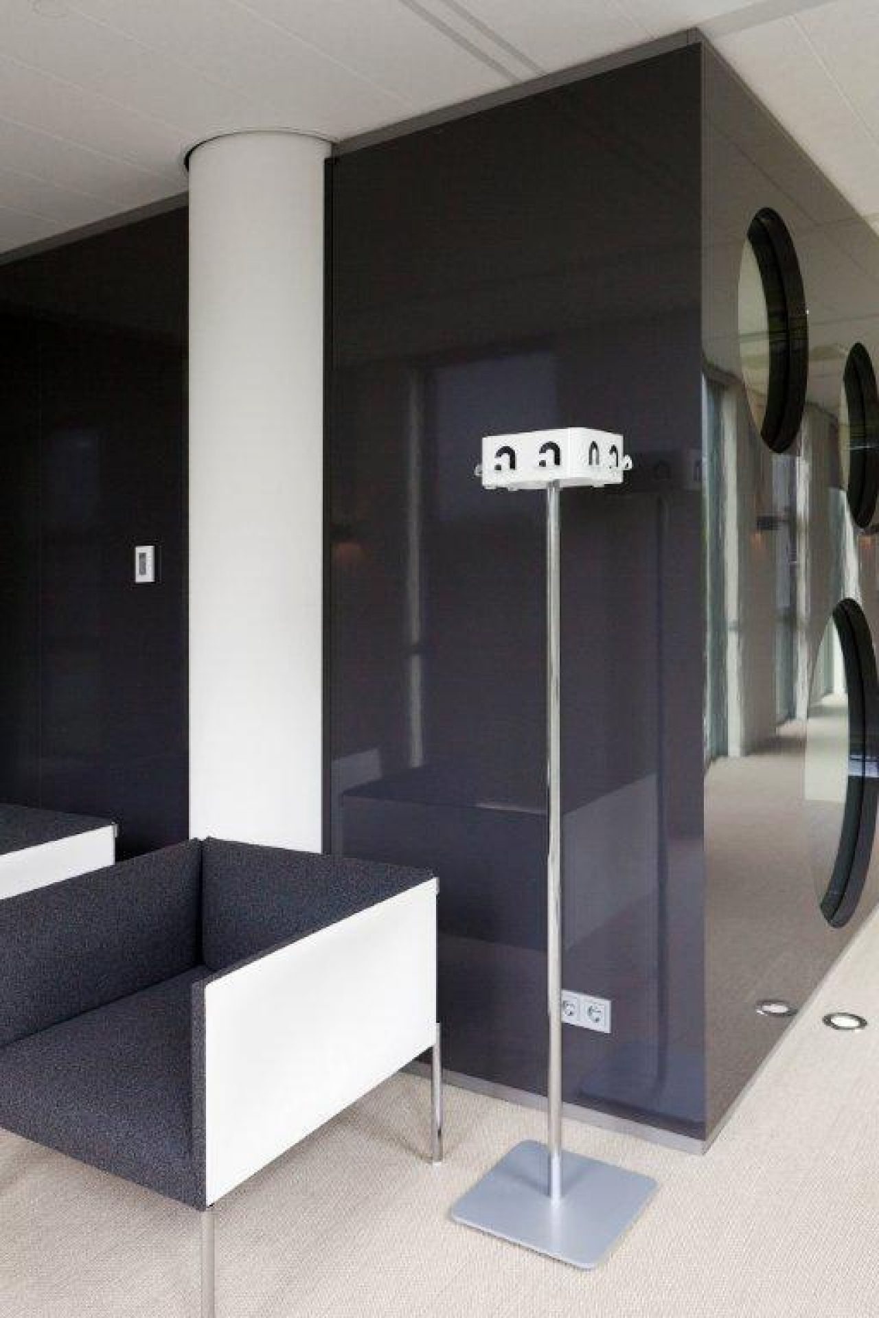 Moderner Wartebereich mit grau-weißem Sessel, Garderobenständer und dunkler Wand mit runden Fenstern für stilvolles Bürodesign.