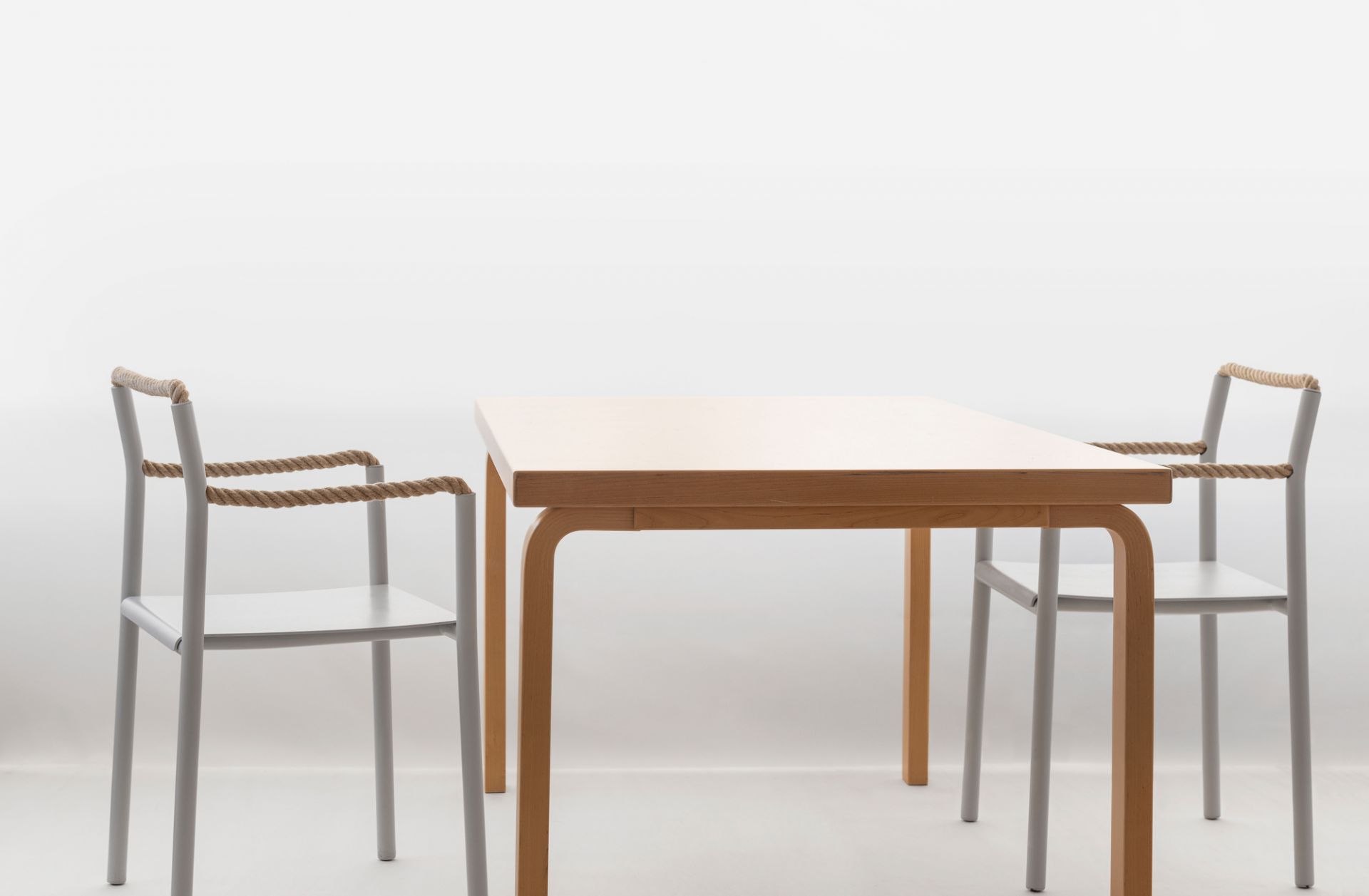 Artek Rope Chair Stuhl mit Tisch: Graue Stühle mit Seil-Armlehnen und Holztisch vor weißem Hintergrund.