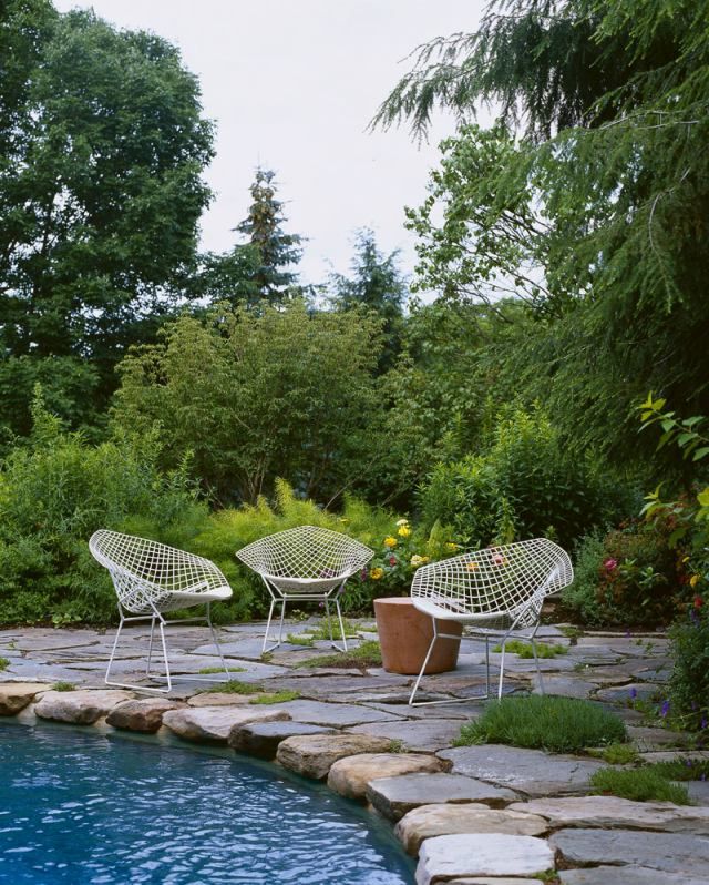 Drei weiße Bertoia Diamond Sessel Outdoor von Knoll International stehen auf einer Terrasse am Pool.