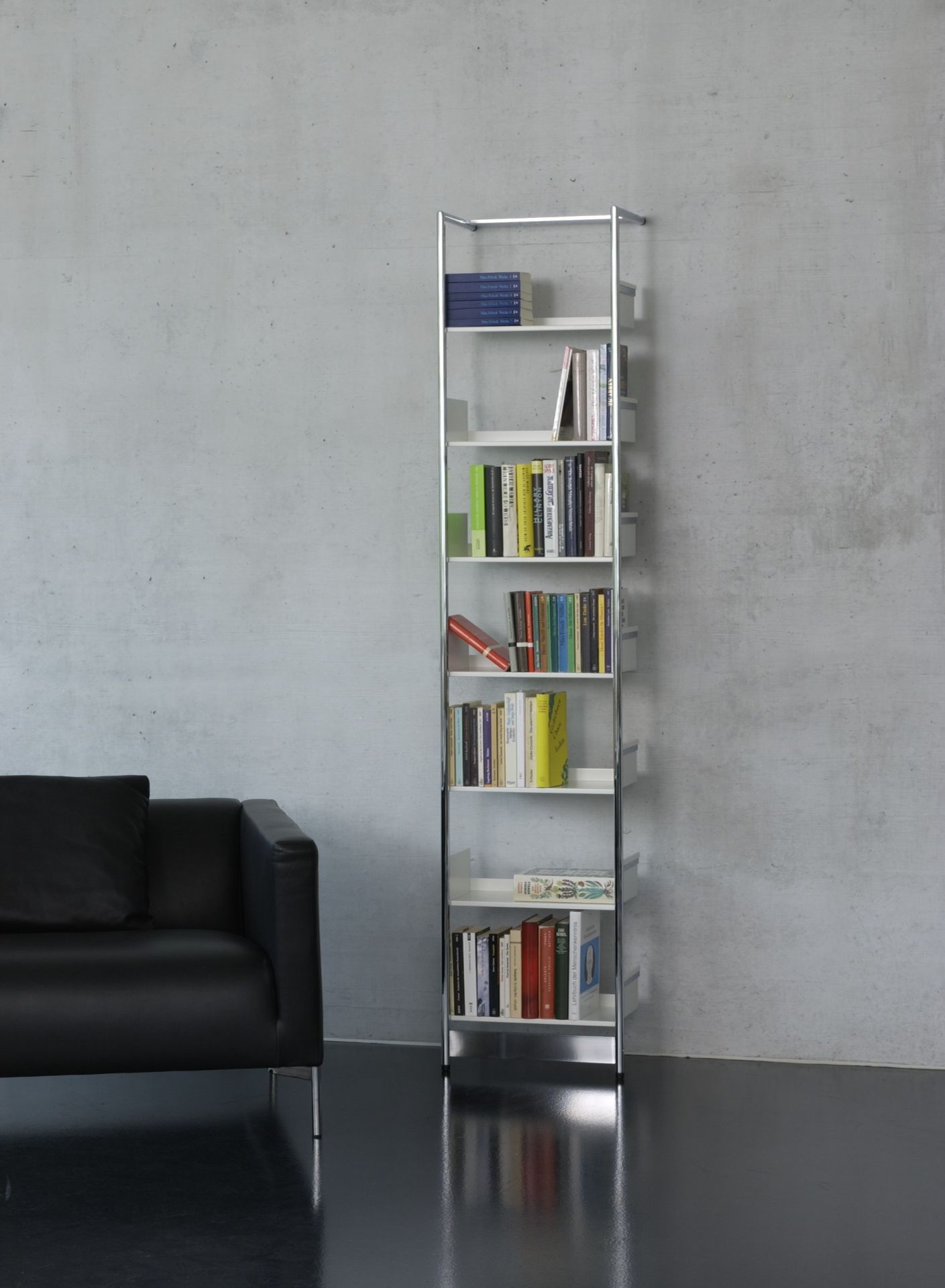 Pool 196 Medium Anlehnregal von Mox, freistehendes Bücherregal aus Stahl und weißen Regalböden, neben schwarzem Sofa.