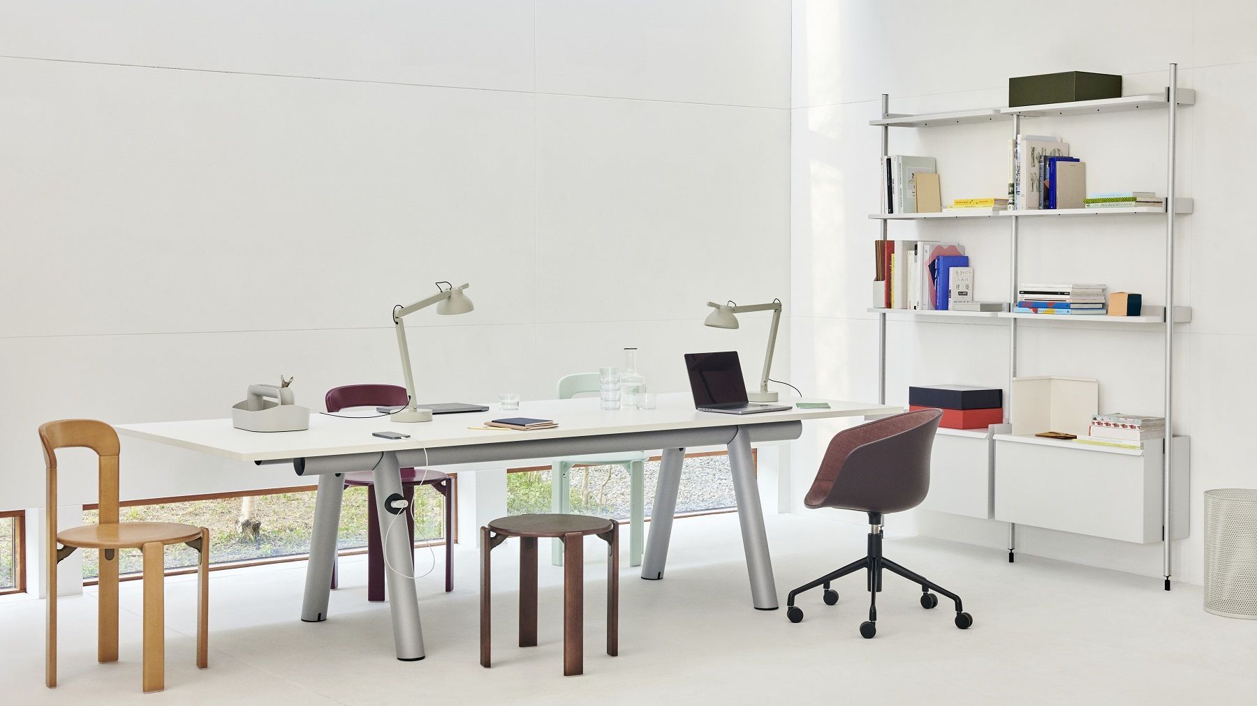 Heller Büroraum mit großem weißen Hay Boa Table, Stühlen, Regalen und zwei Schreibtischlampen.