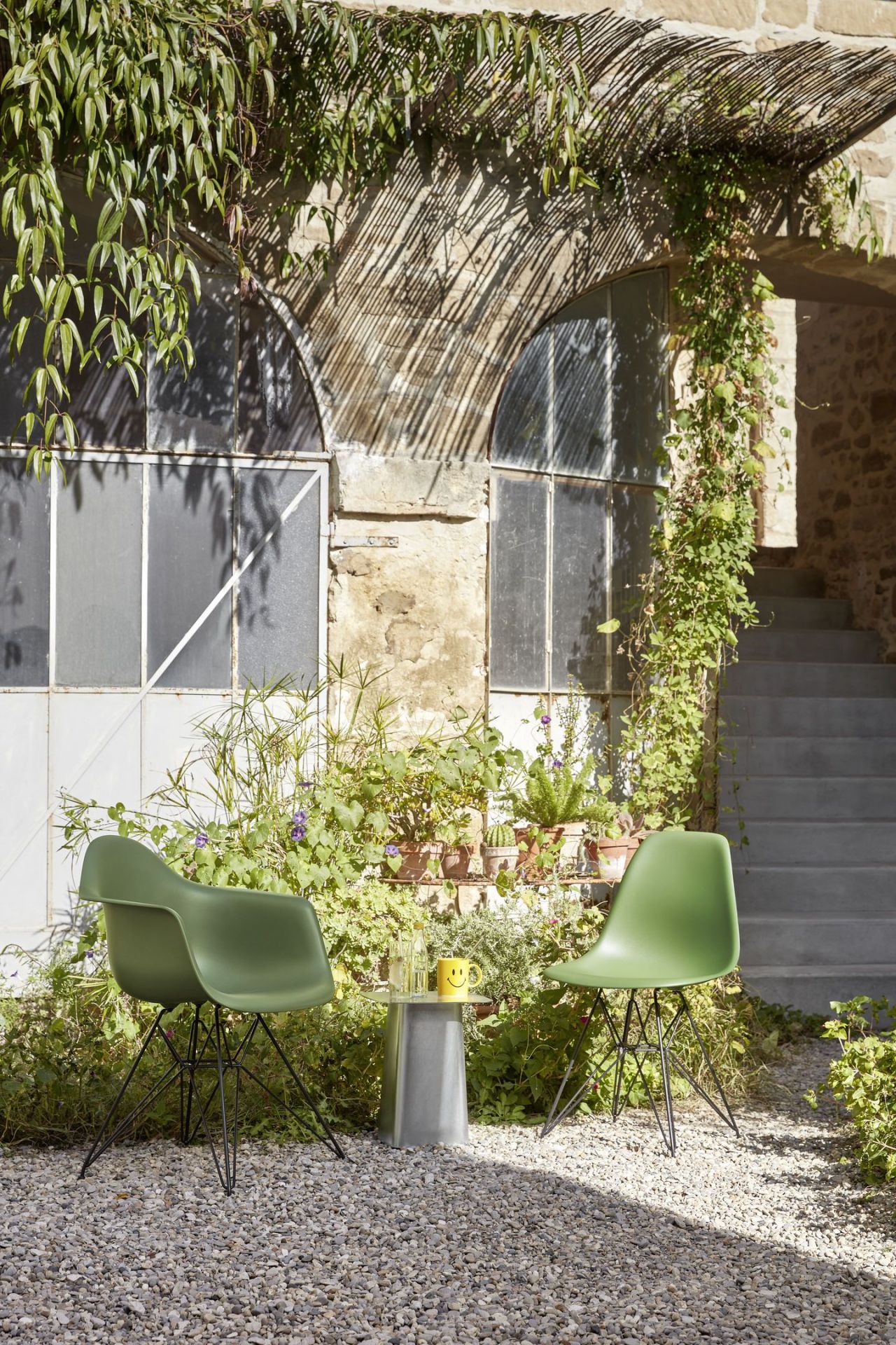 Zwei grüne Eames DSR Stühle von Vitra mit schwarzem Gestell im Außenbereich mit Pflanzen.