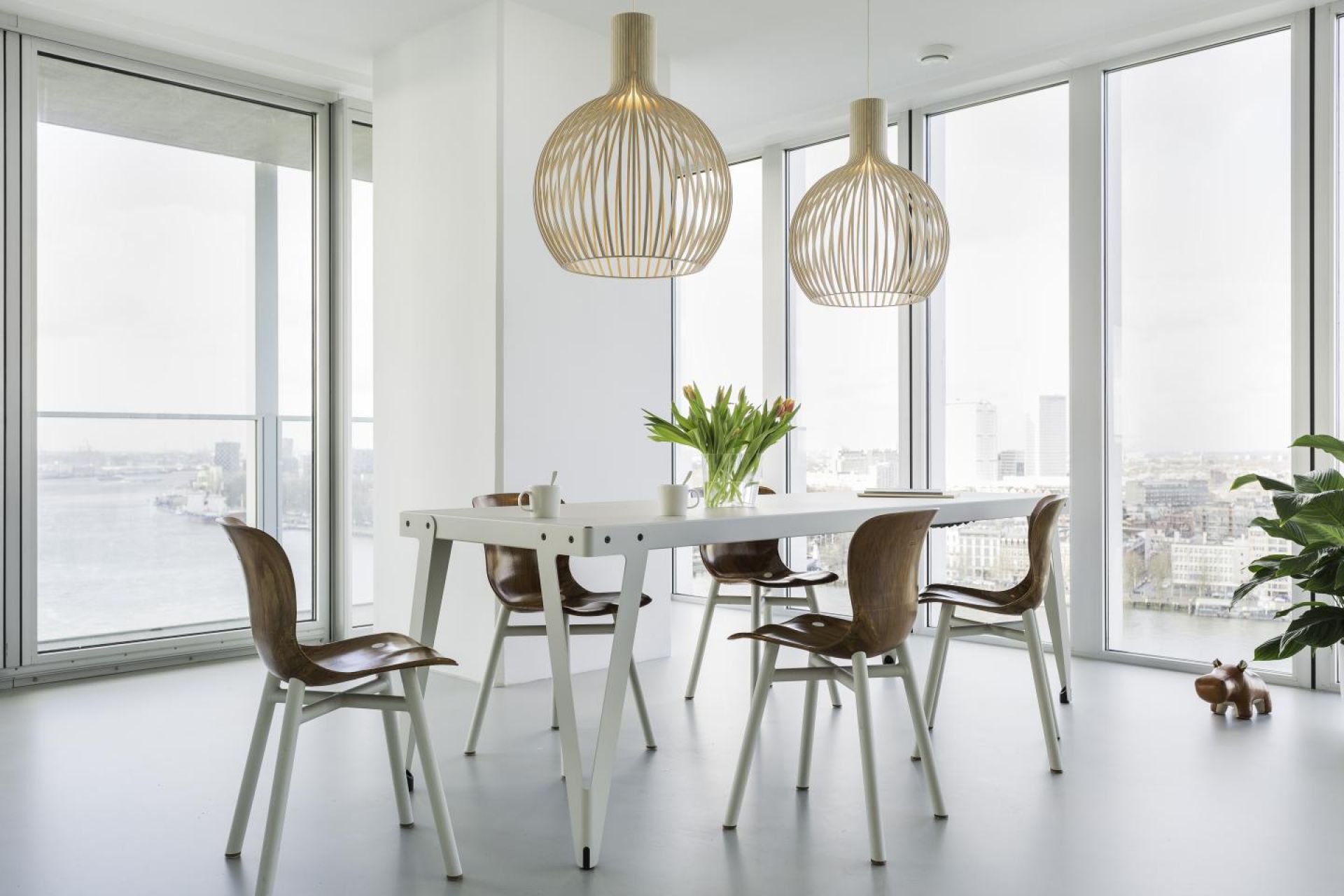 Esszimmer mit Lloyd Indoor Table Tisch, Holzstühlen und modernen Pendelleuchten vor Fensterfront.
