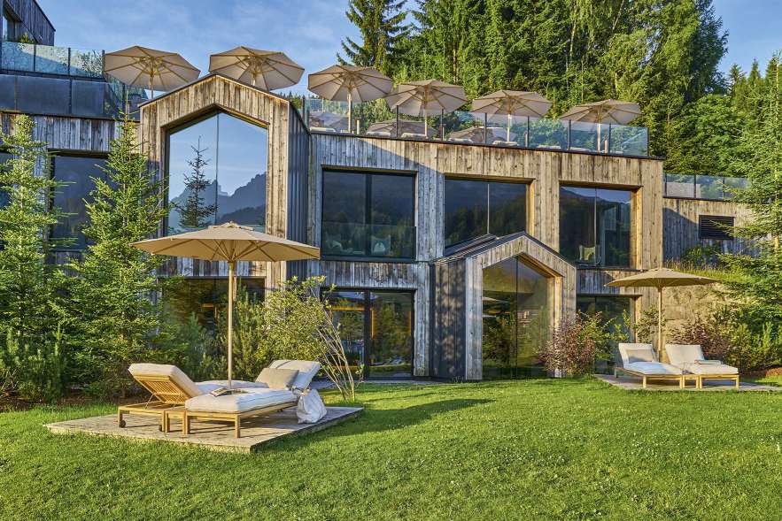 Weishäupl Klassiker Sonnenschirme auf dem Dach und im Garten eines modernen Holzhauses mit Liegestühlen.