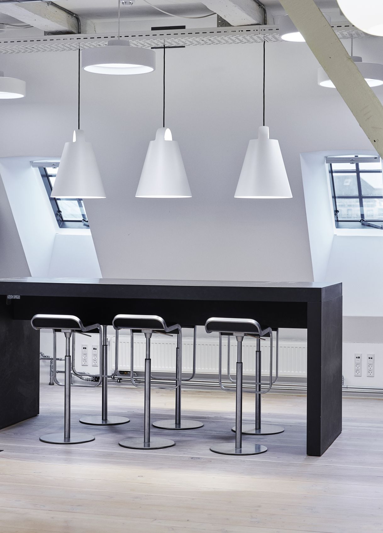 Drei weiße Above Pendelleuchten von Louis Poulsen über einem schwarzen Tisch mit Barhockern.