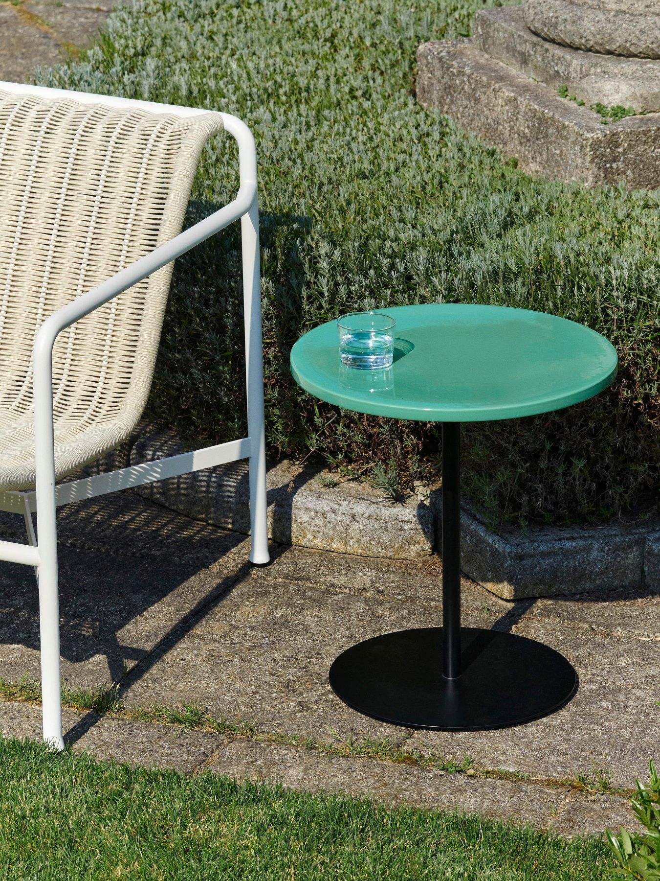 Hay Pyro Coffee Table Outdoor in Grün mit schwarzem Fuß und Glas Wasser neben Stuhl.