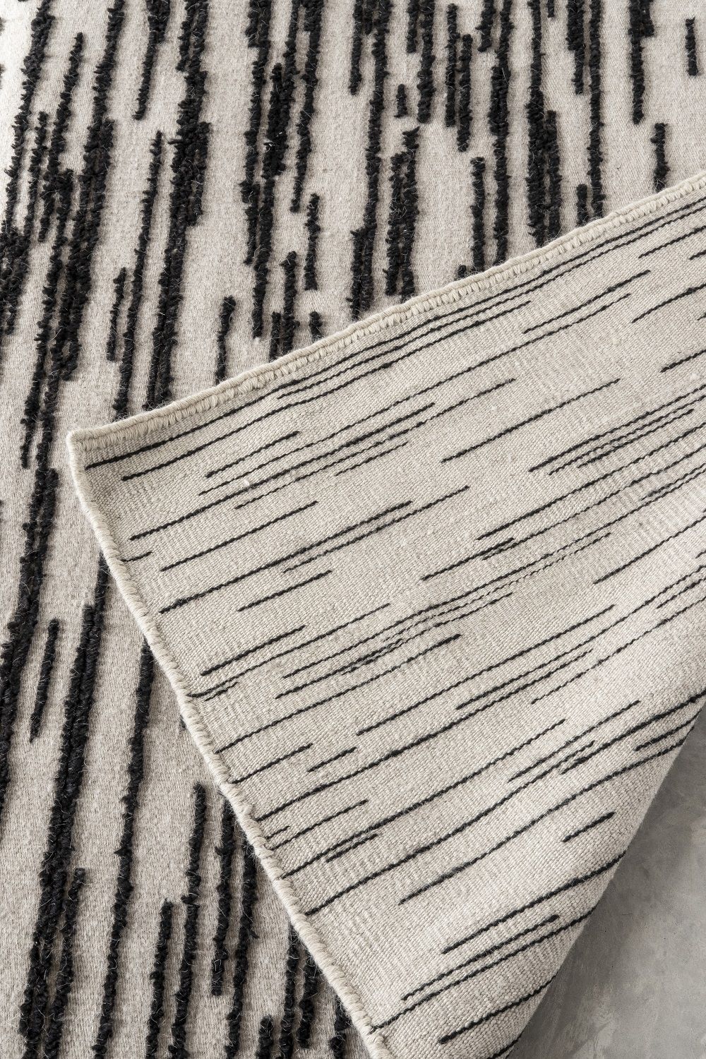 Detailaufnahme des Nanimarquina Doblecara Rug Teppichs mit abstraktem, schwarzen Linienmuster auf beiger Textur.
