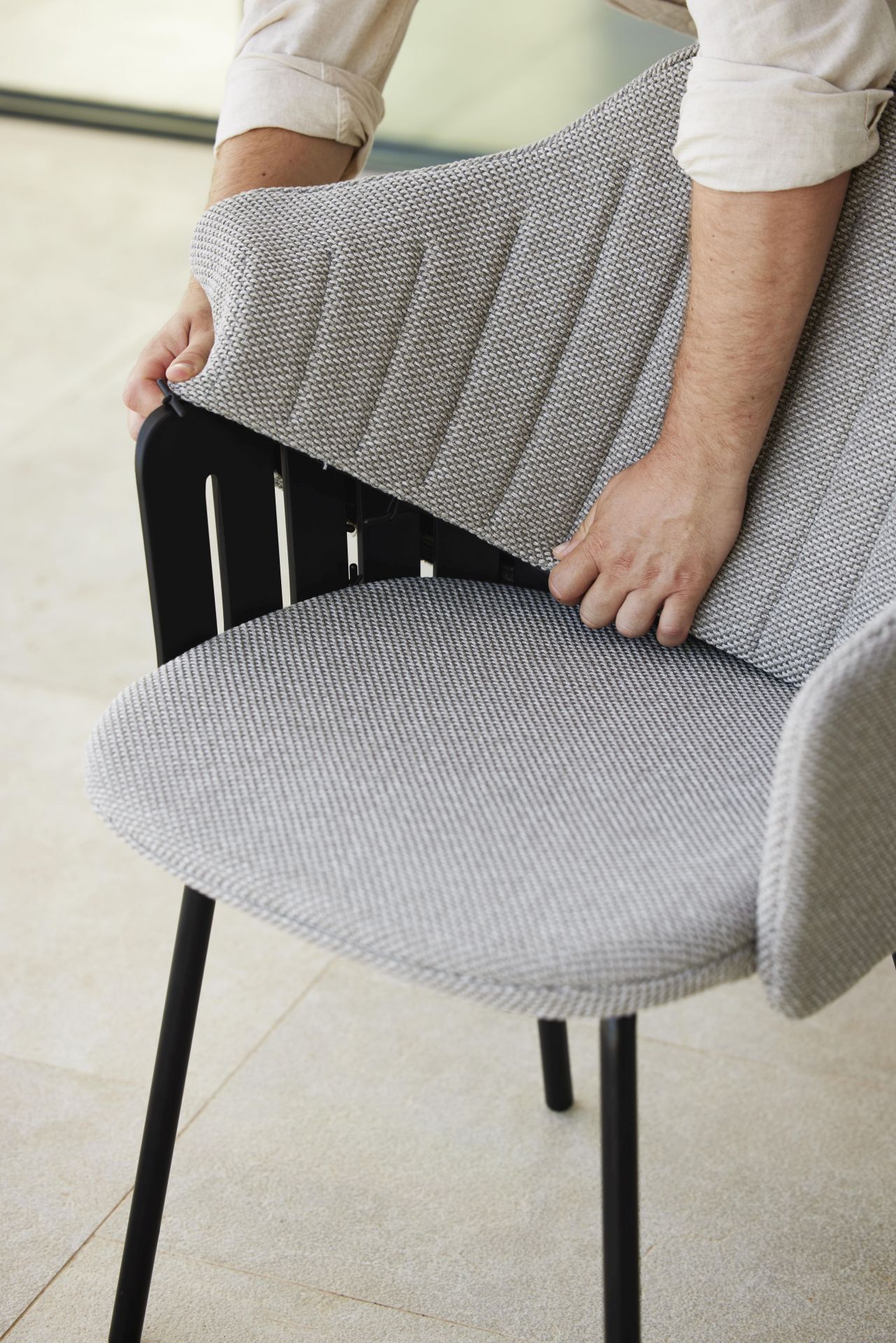 Mann befestigt Choice Sitzkissen in Taupe von Cane-Line an einem Outdoor Stuhl.