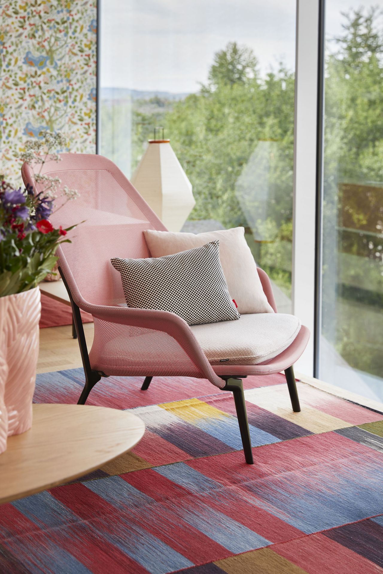 Vitra Slow Chair Sessel in Rosa mit Kissen und Ottoman vor Fenster mit Gartenblick.