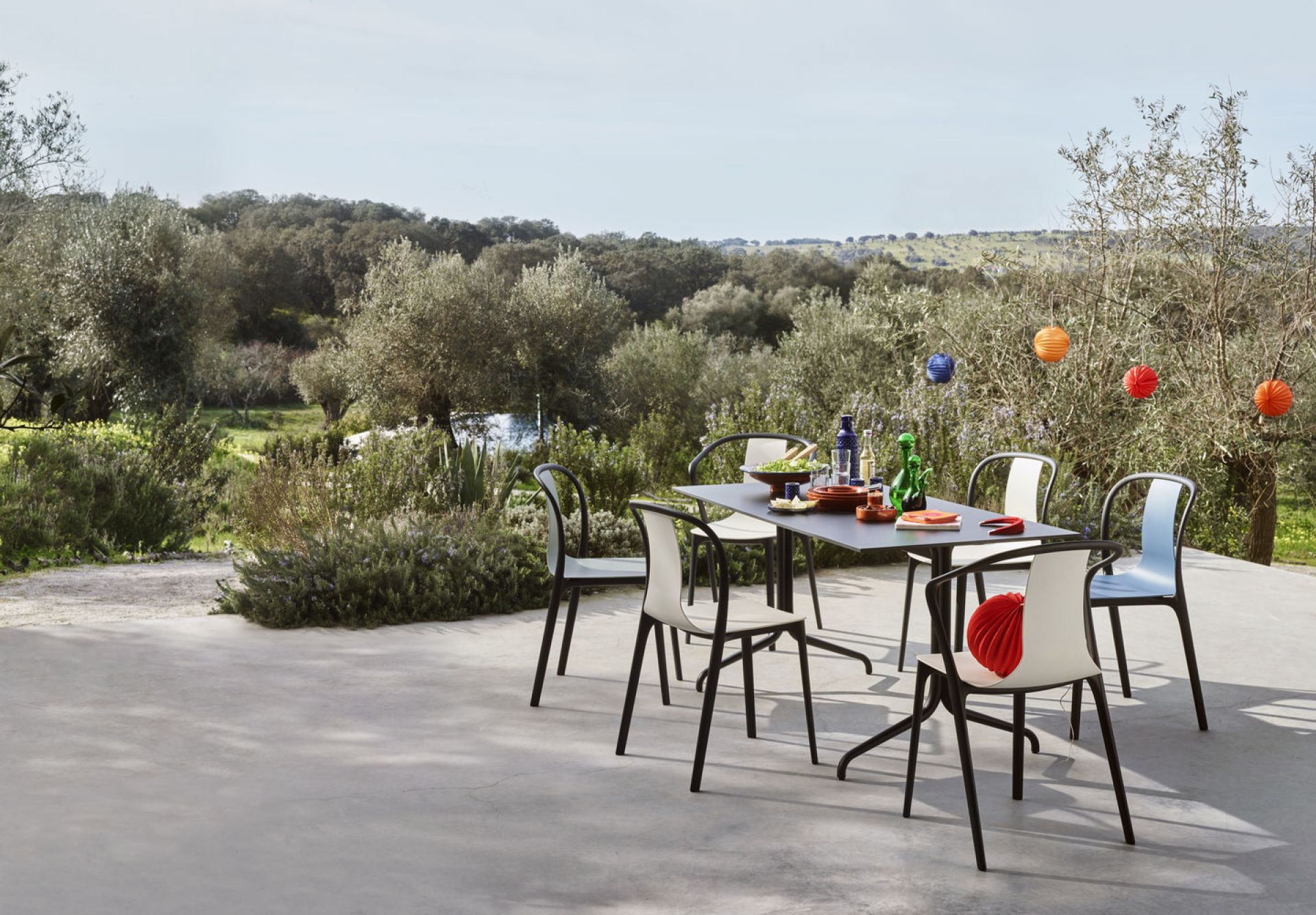 Vitra Belleville Armchair Plastic Stühle um einen Esstisch im Freien mit Garten im Hintergrund.