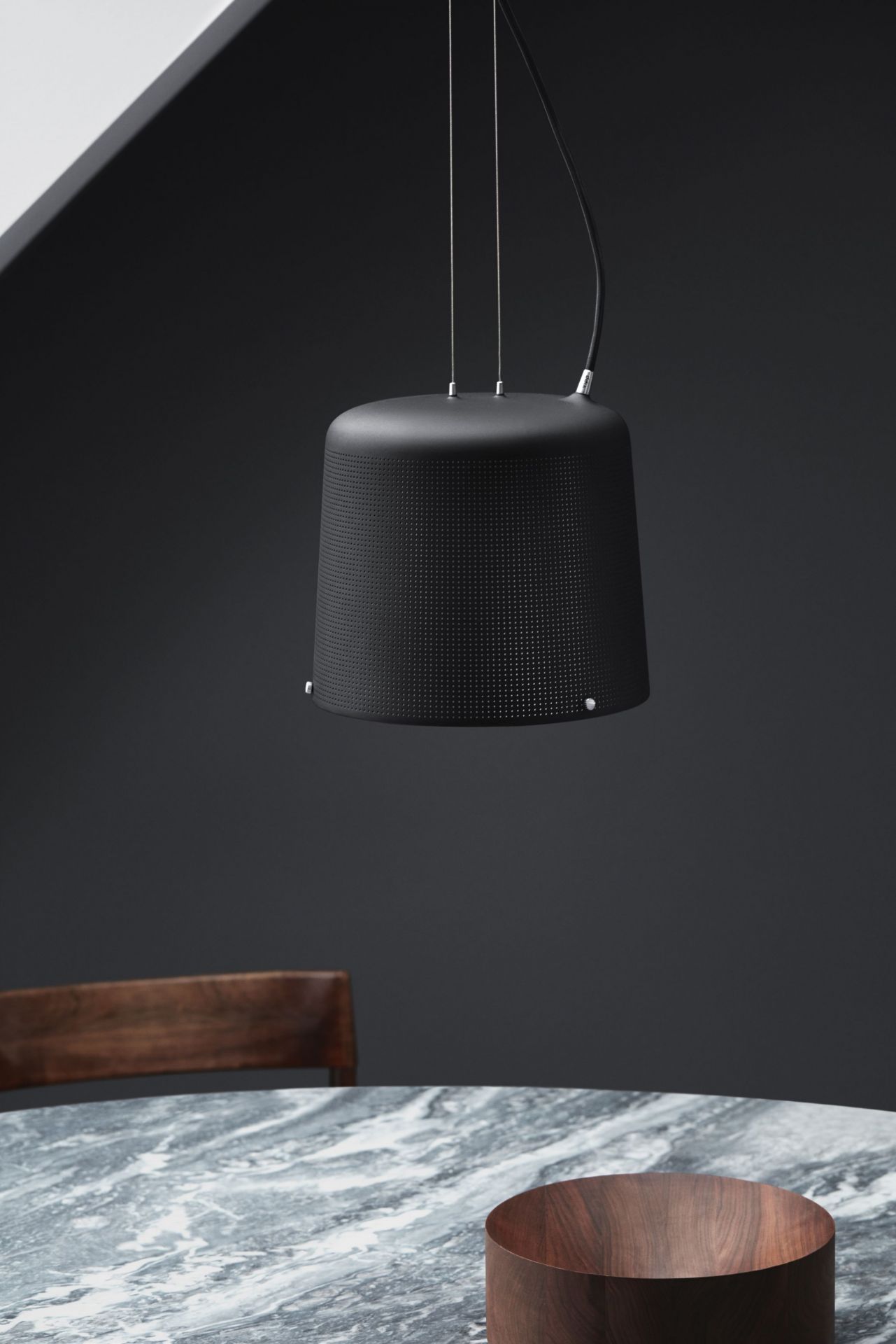 Schwarze Vipp Pendelleuchte mit feinen Löchern über einem Marmortisch und Holzschale.