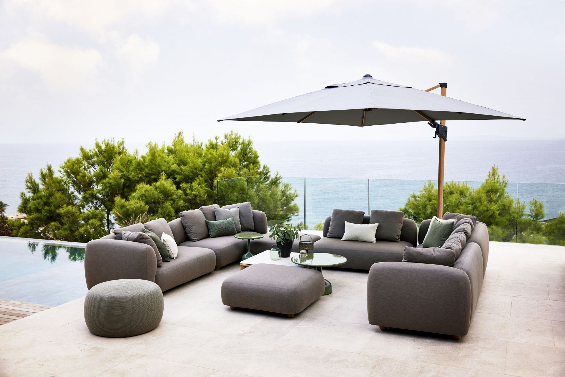 Capture Outdoor Sofa von Cane-Line, graue Lounge-Möbel mit Kissen und Beistelltischen auf einer Terrasse.