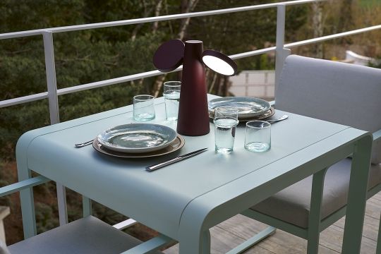 Lakritzfarbene Oto Tischleuchte von Fermob auf einem gedeckten Gartentisch im Freien.
