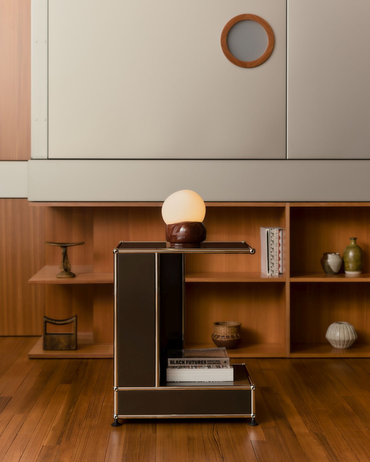 USM Haller Beistelltisch Arkad Edition in Braun mit Lampe und Büchern vor Holzregal.