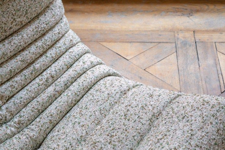 Detailaufnahme des Togo Sessel ligne roset mit beigem Stoffbezug und Falten auf einem Holzboden.