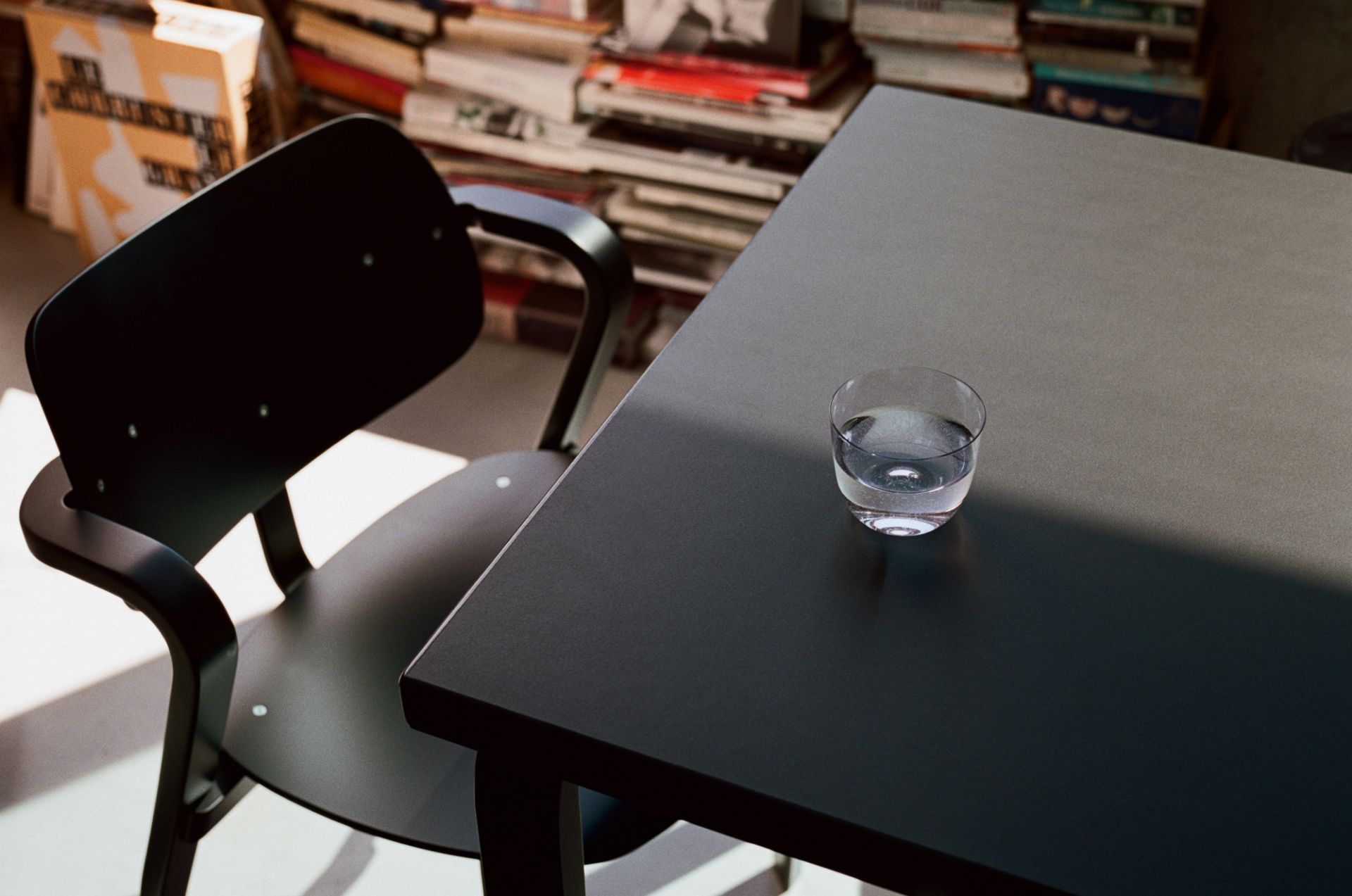 Grau lackierter Aslak Chair Stuhl von Artek neben einem Tisch mit einem Wasserglas.