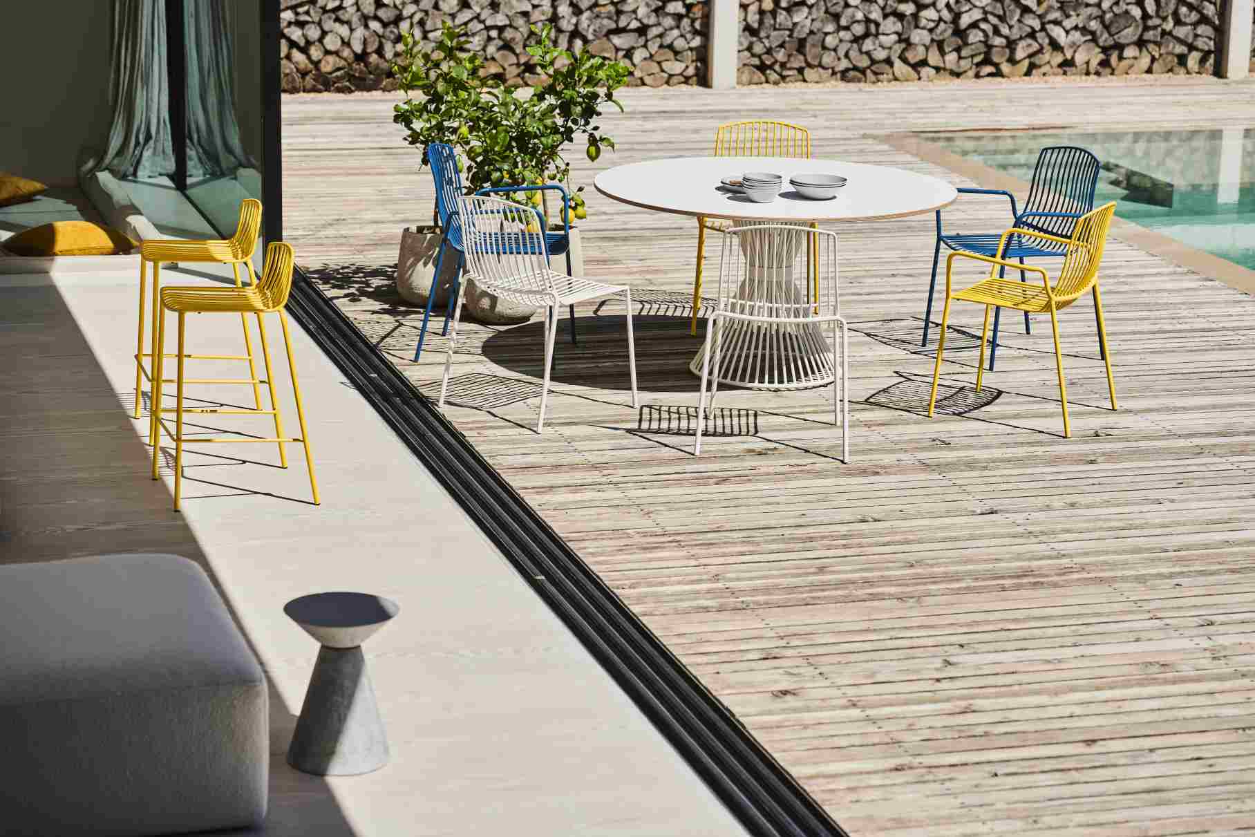 Mori Stuhl Outdoor Jan Kurtz: Mehrfarbige Gartenstühle aus Metall um einen runden Tisch.