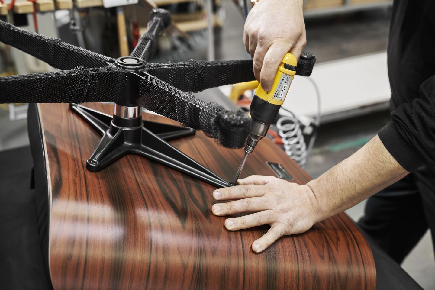 Eames Lounge Chair Montage: Handwerker befestigt das Untergestell am Holzrahmen des Sessels mit Akkuschrauber.