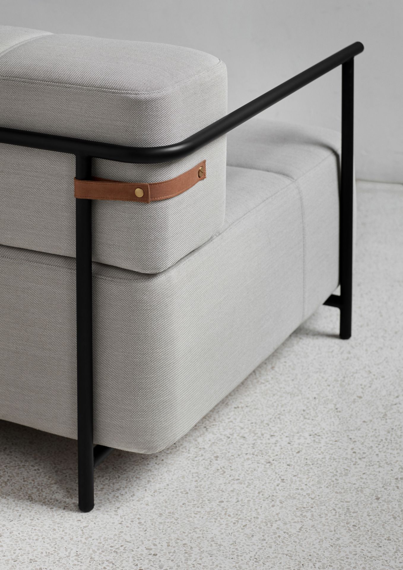 Detailaufnahme: Graues Daybe Schlafsofa mit Armlehnen, schwarzem Gestell und Lederdetails.