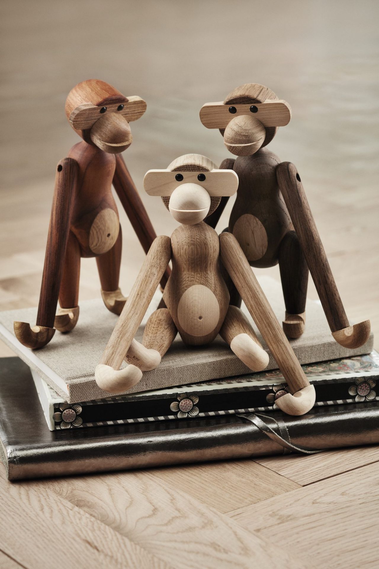 Drei Kay Bojesen Holzfiguren Affen in Eiche geräuchert und Natur auf einem Bücherstapel.